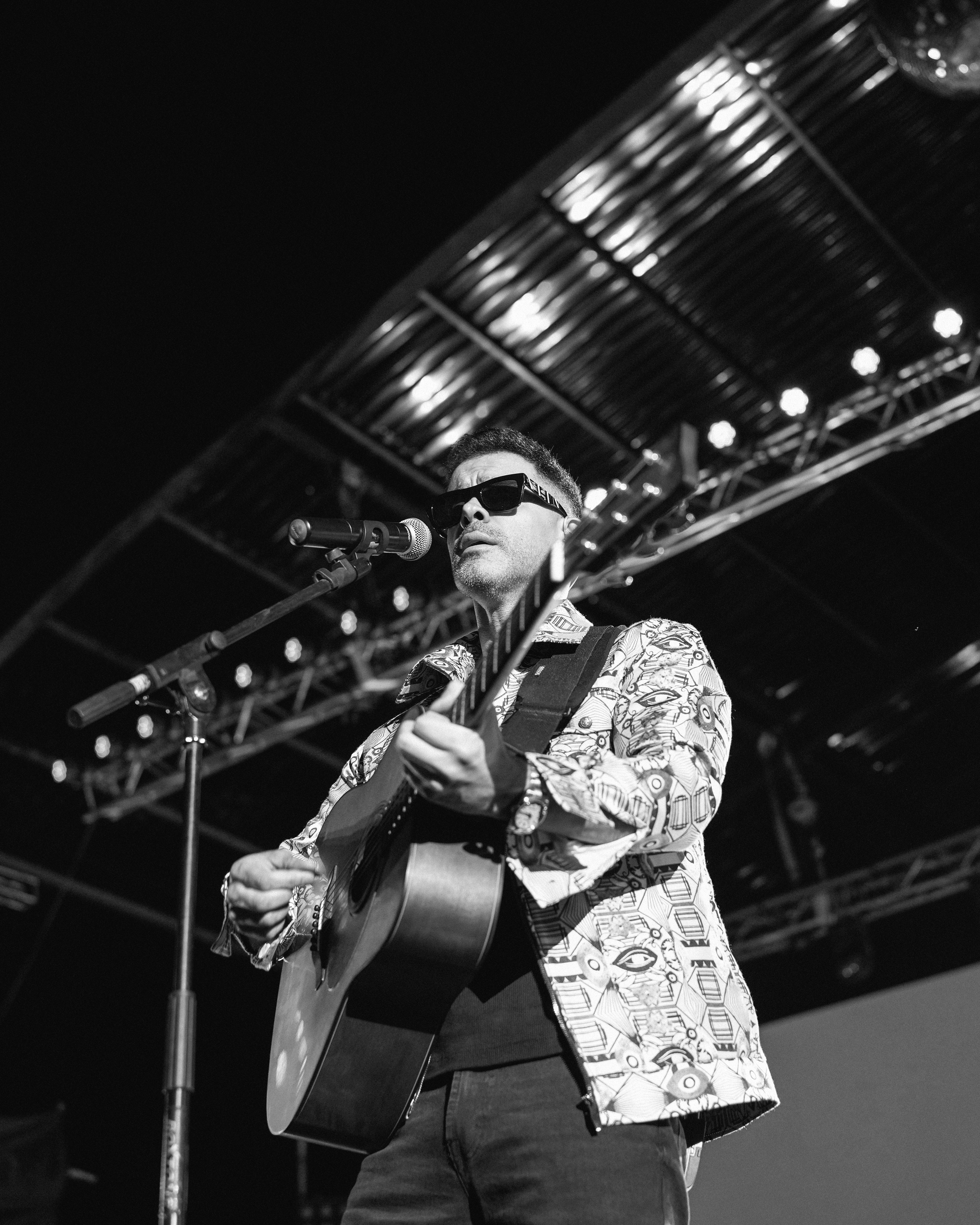 Man playing guitar on stage with sunglasses.