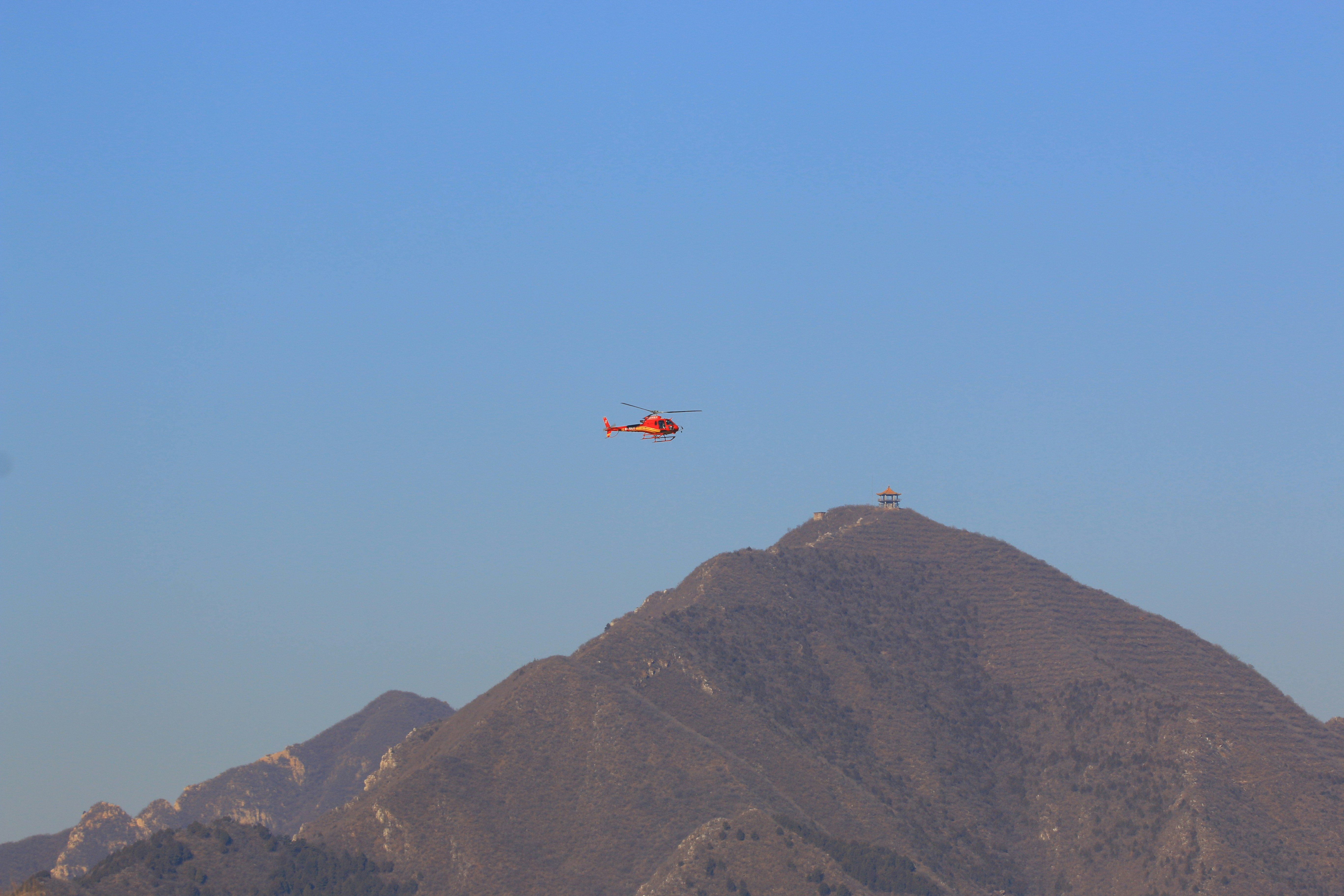 Orange helicopter flies over mountain peak.