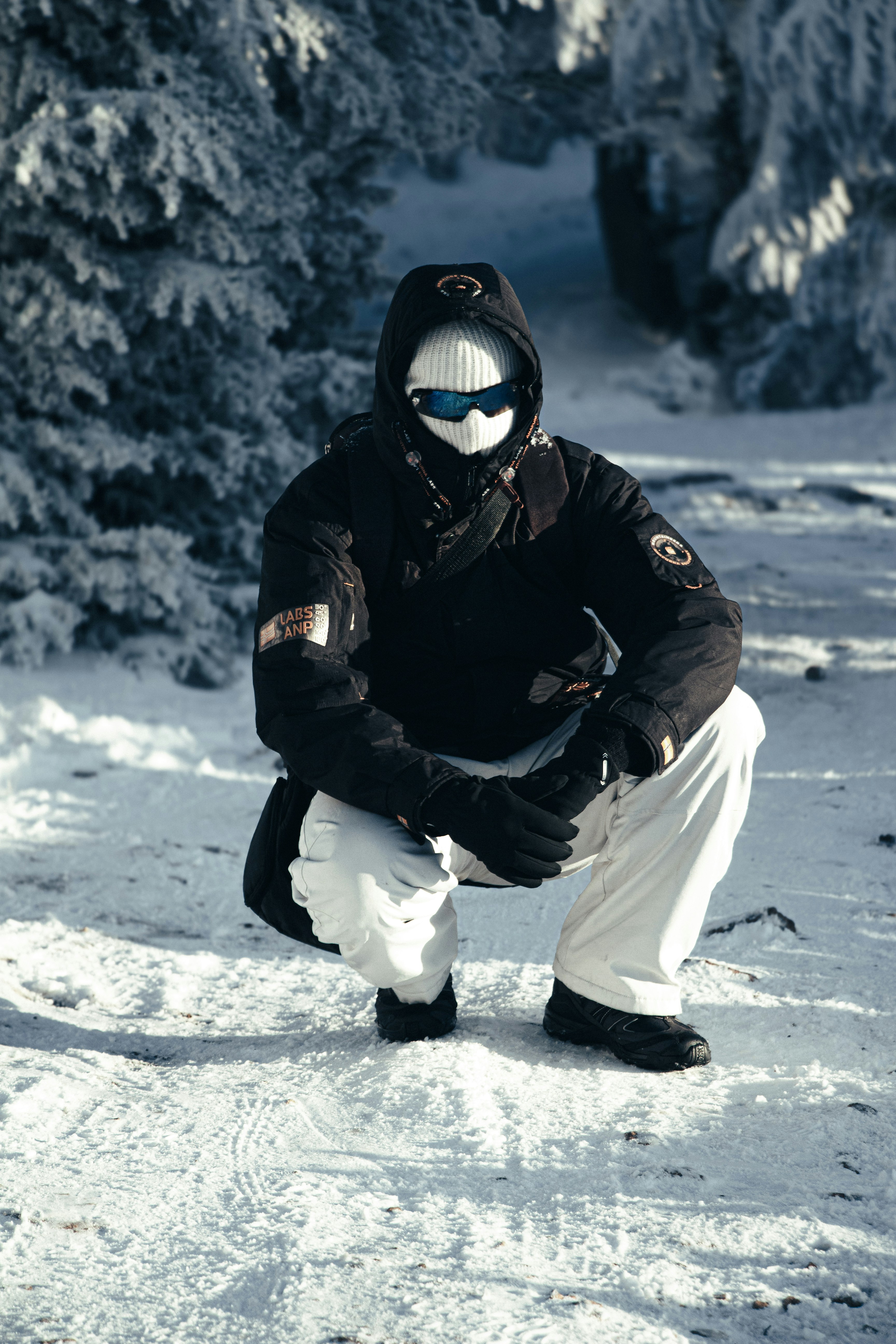 Person in winter gear crouching in snowy forest