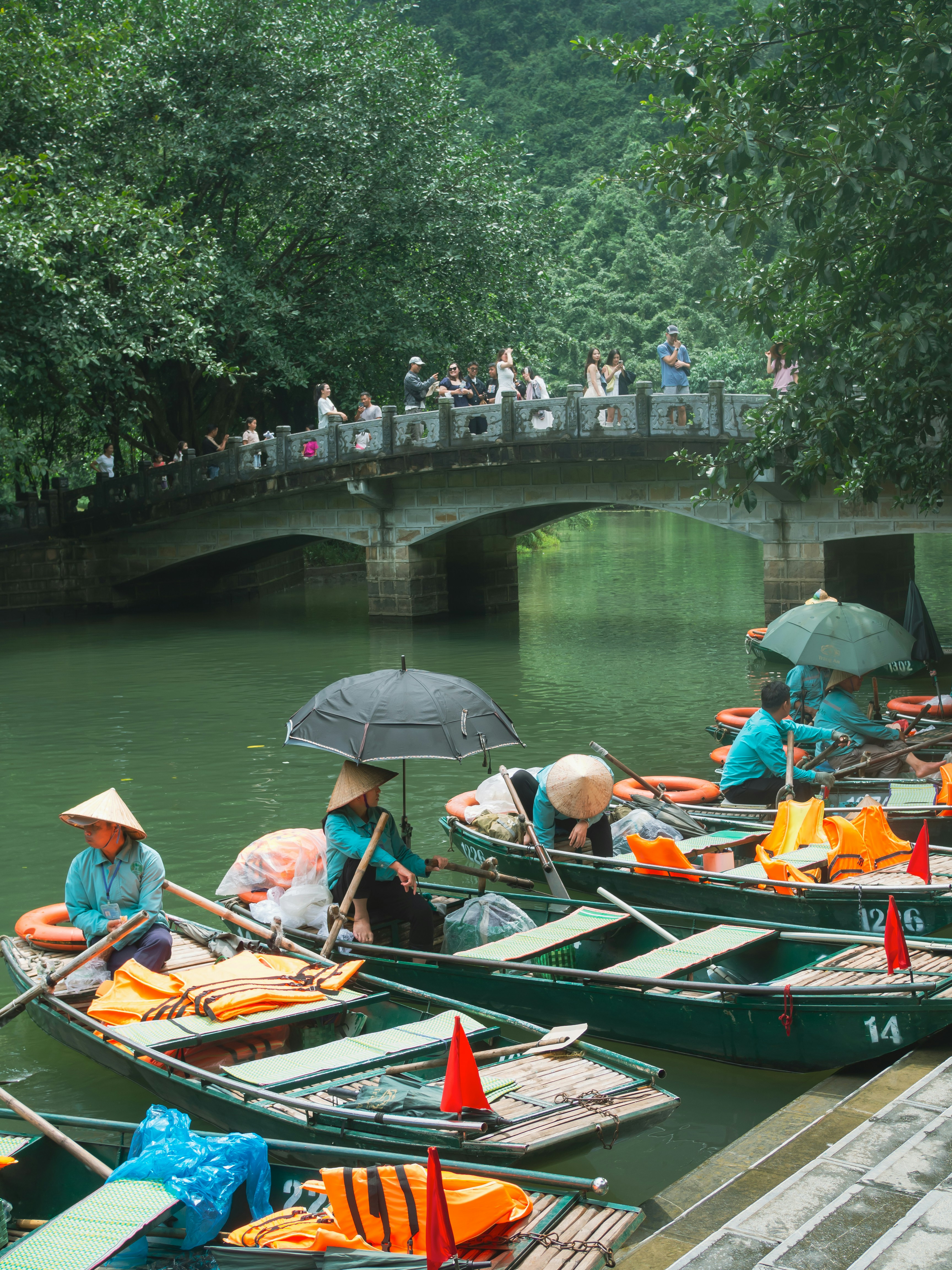Boats with people under umbrellas near a bridge