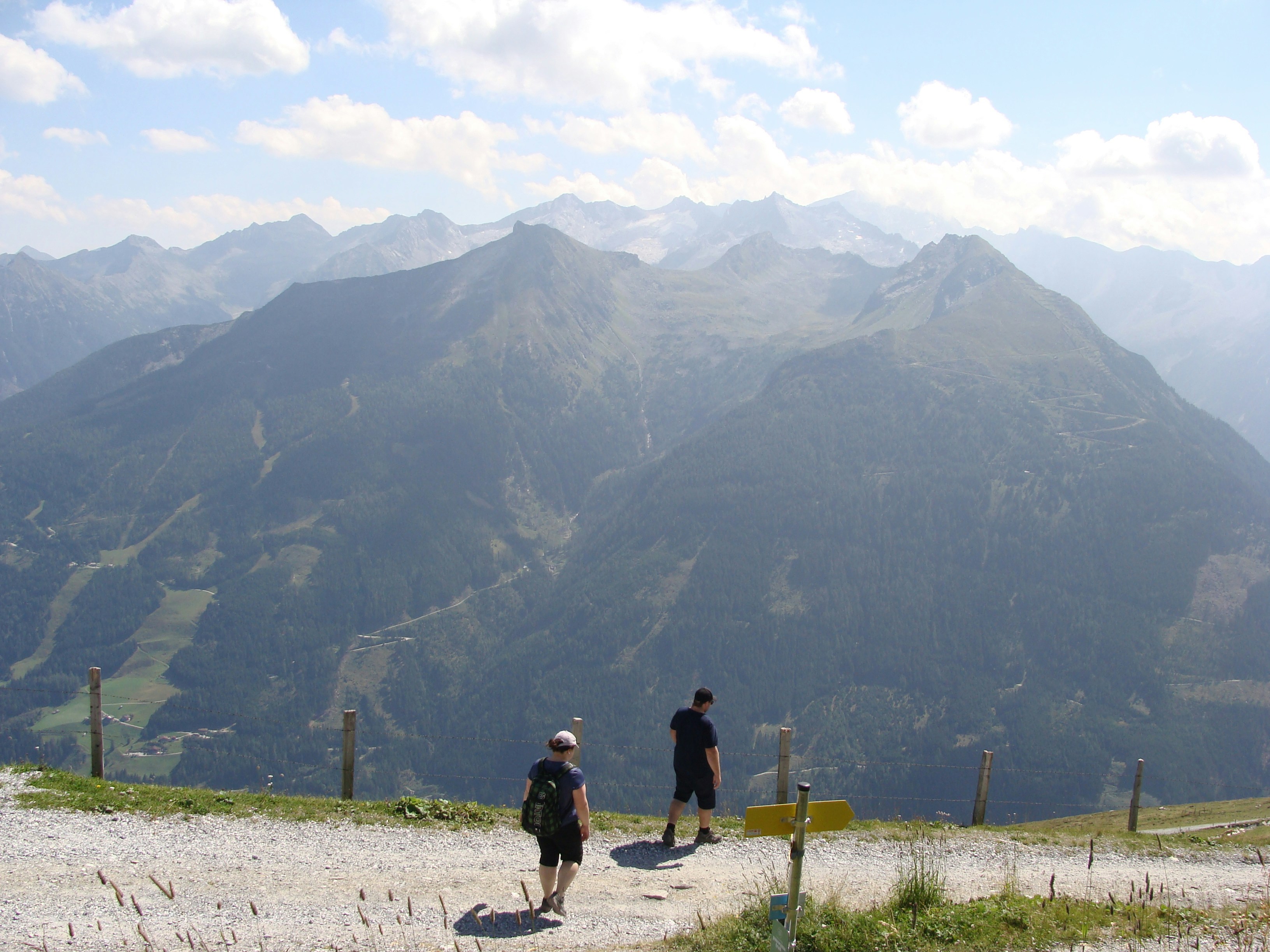 Two runners on a high mountain trail overlooking vast alpine peaks