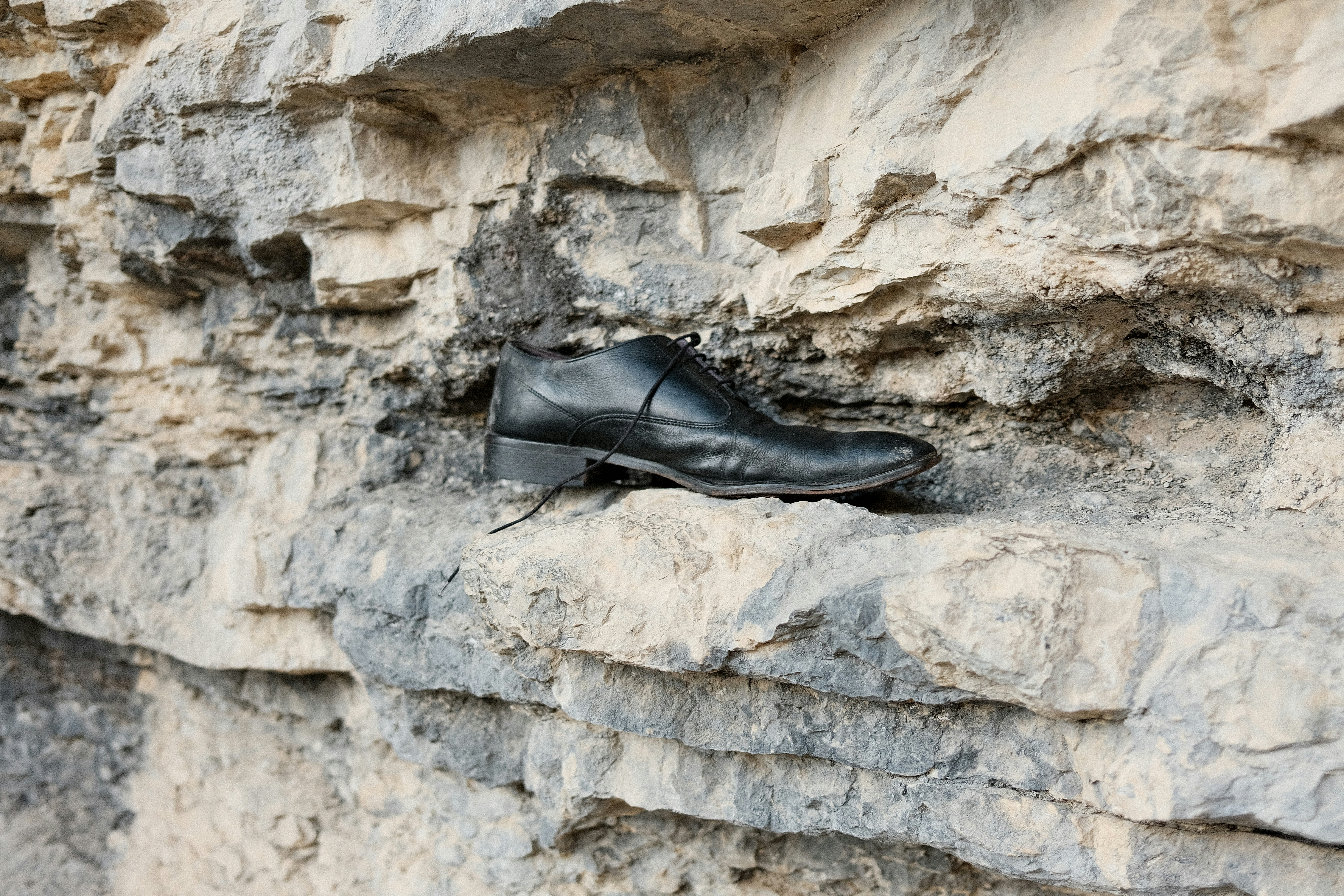 A single black dress shoe rests on a rock ledge.