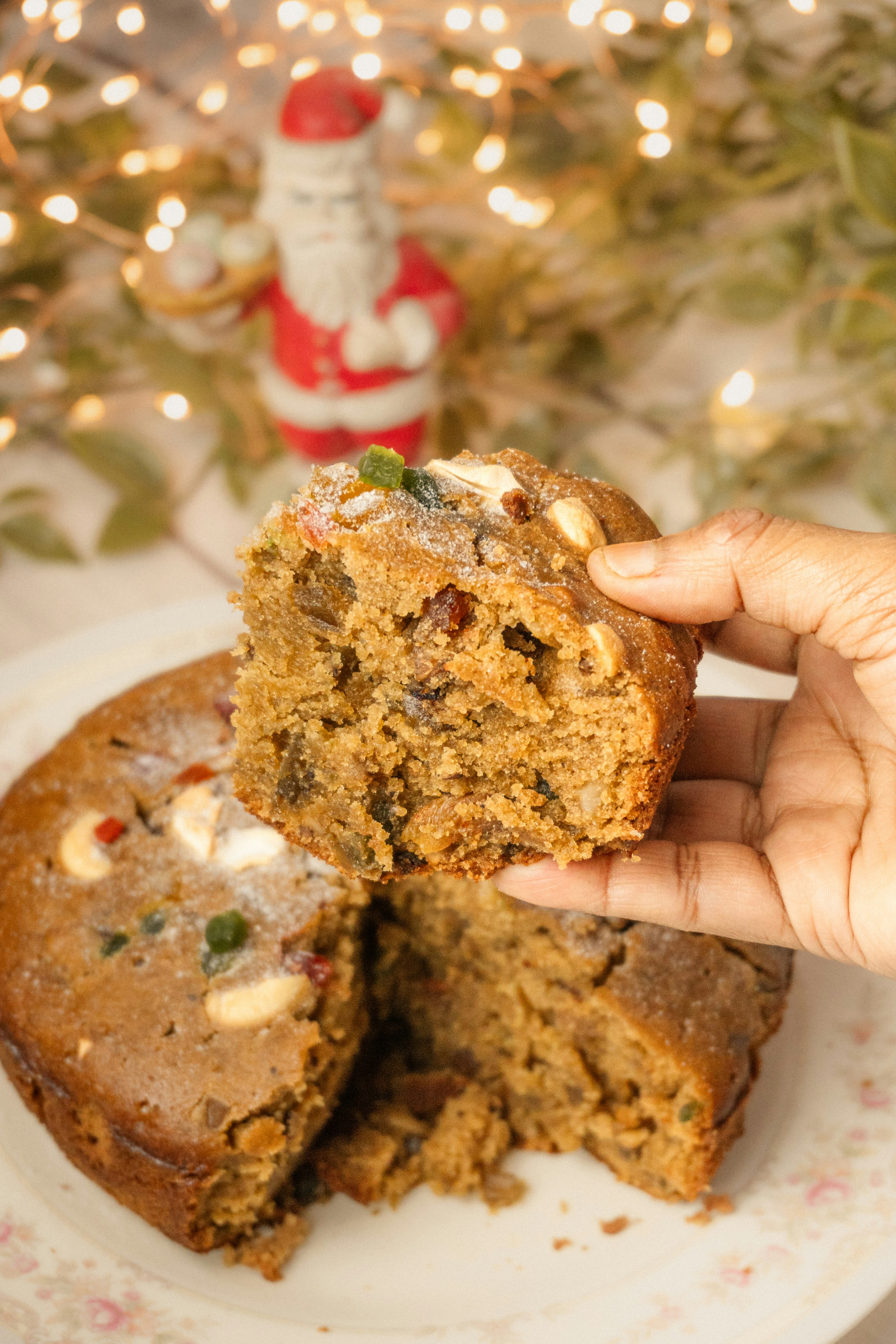 Hand holding slice of fruitcake with christmas decorations