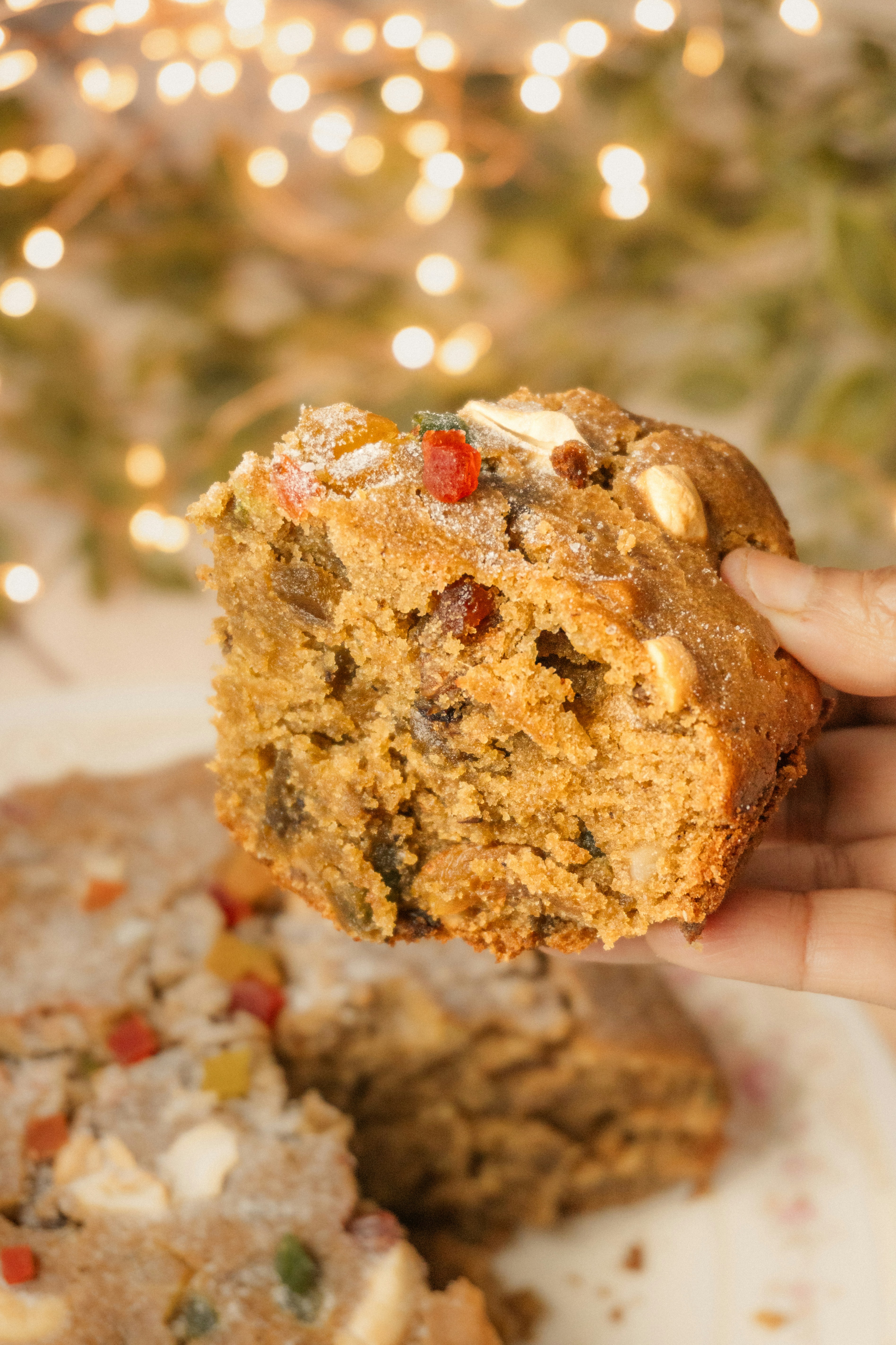 Hand holding a slice of fruitcake with festive lights