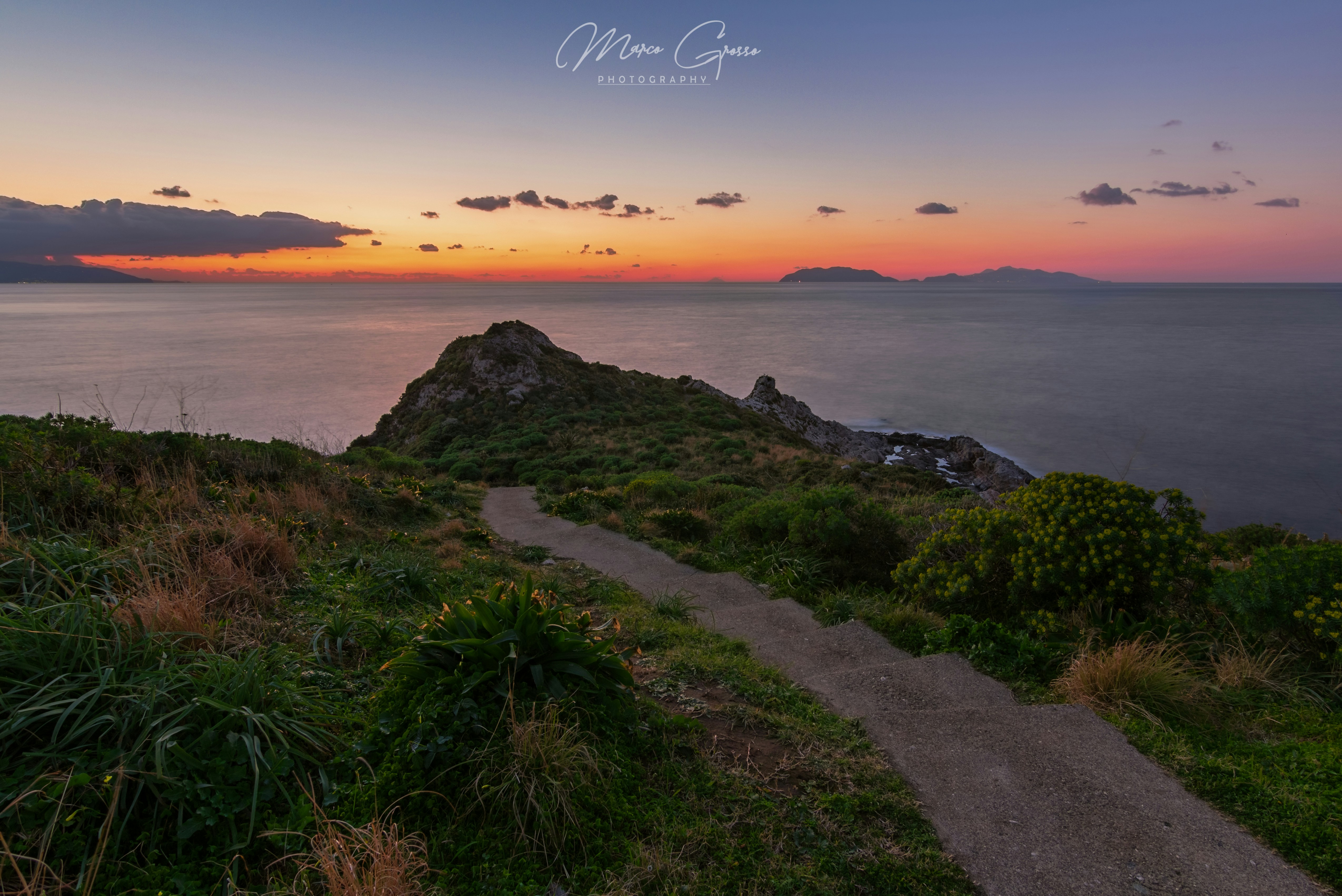 Coastal path leading to a rocky outcrop at sunset
