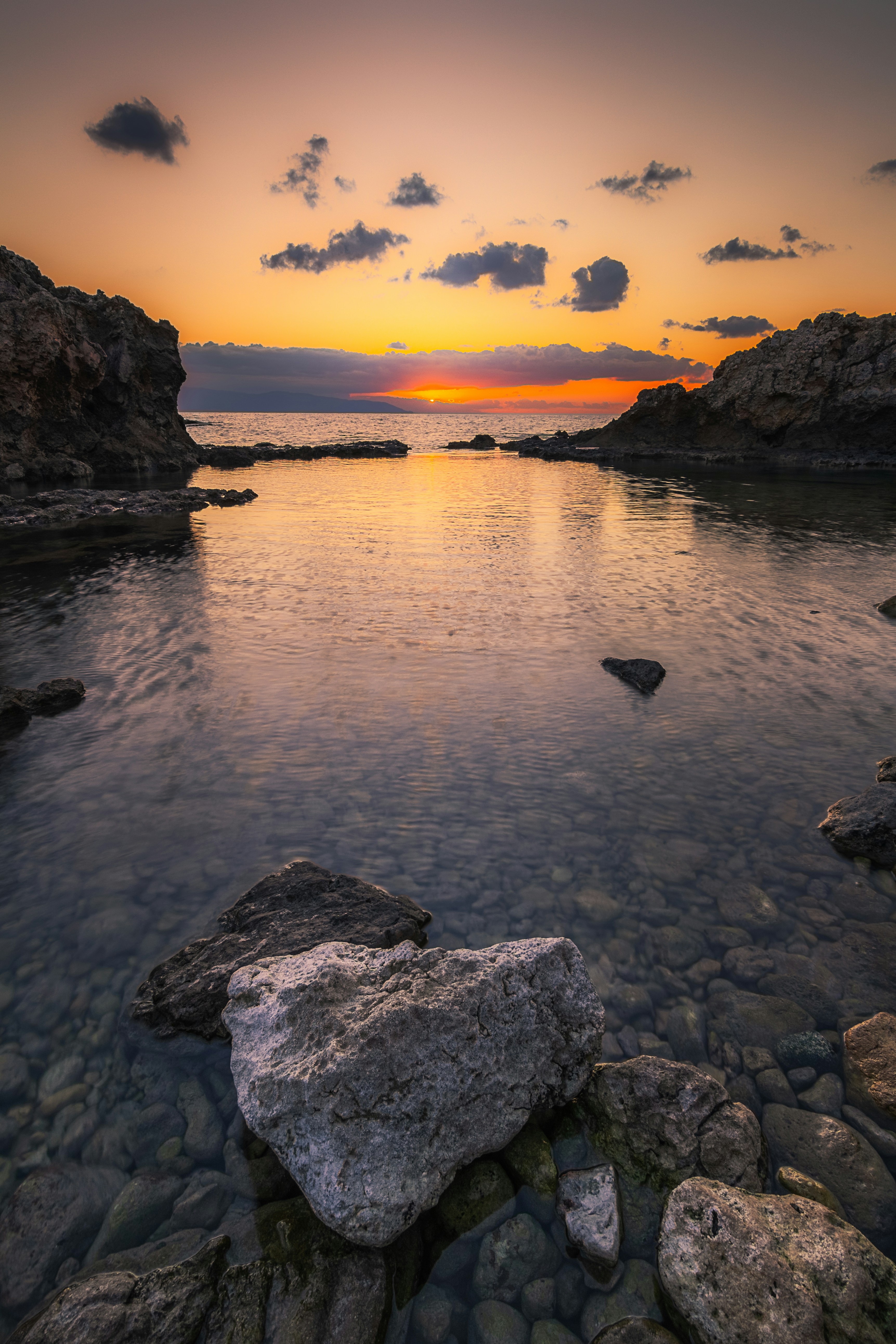 Sunset over a calm ocean with rocky shores.