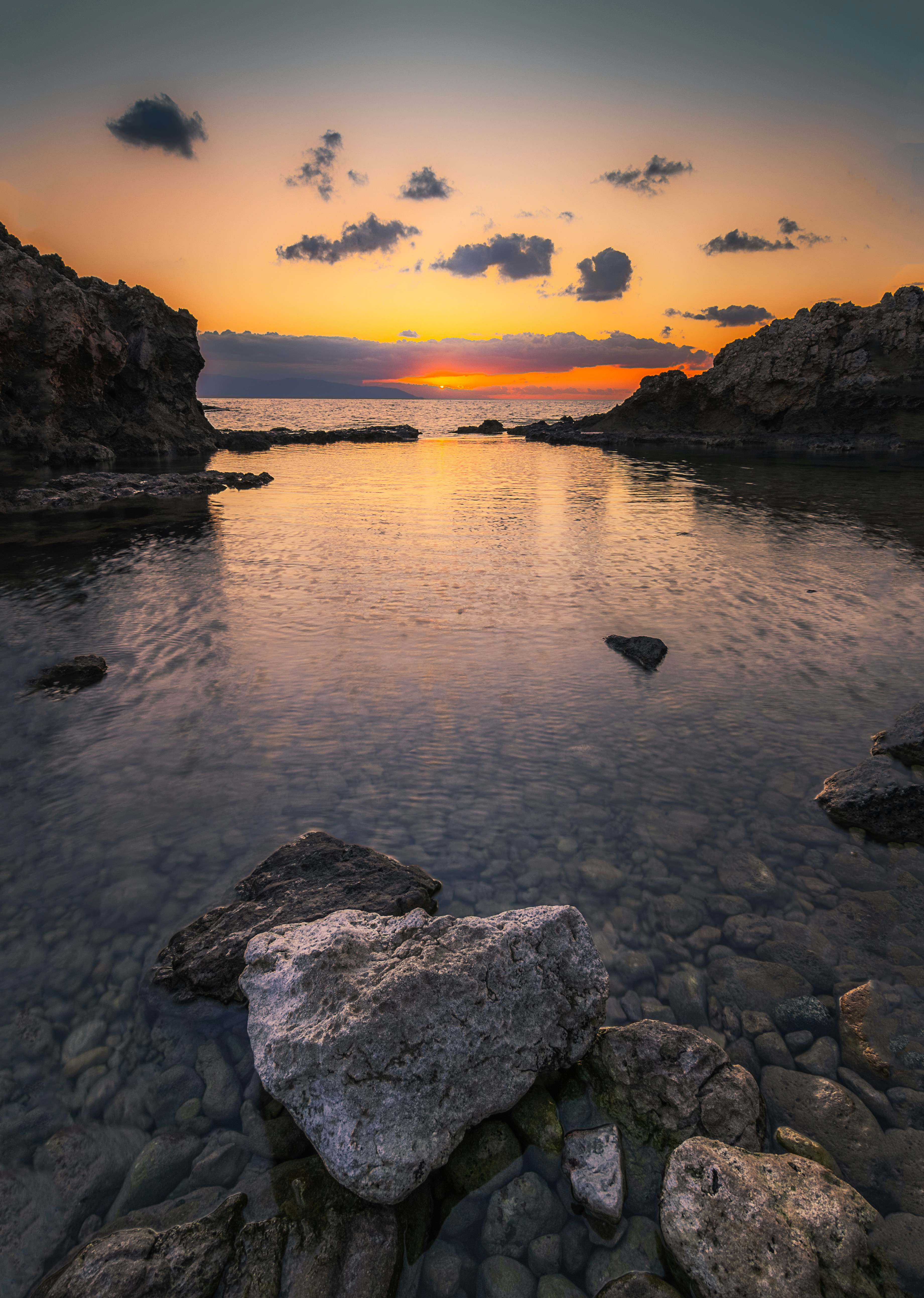 Sunset over a calm ocean with rocky shores
