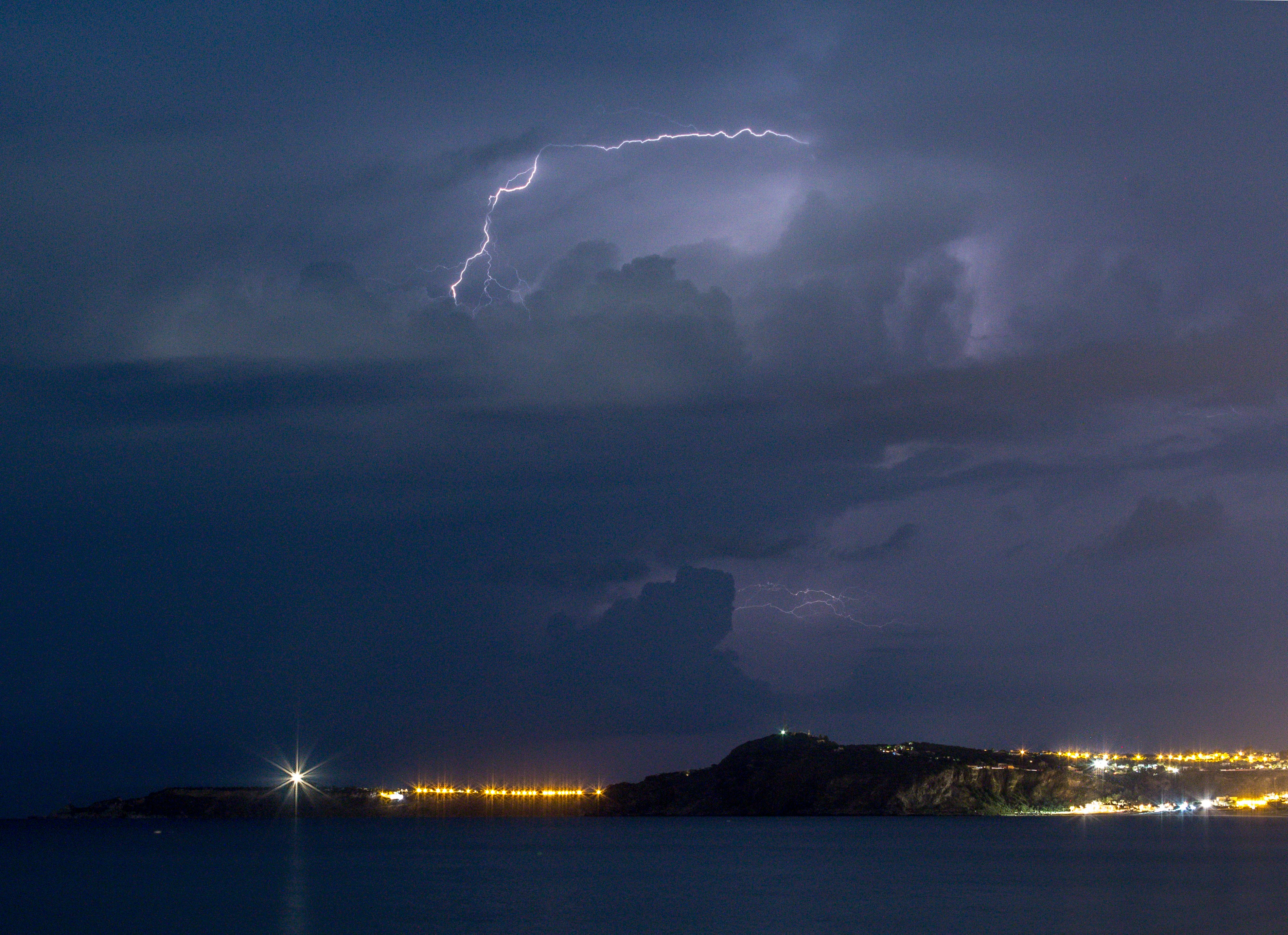 Lightning strikes over a coastal town at night.