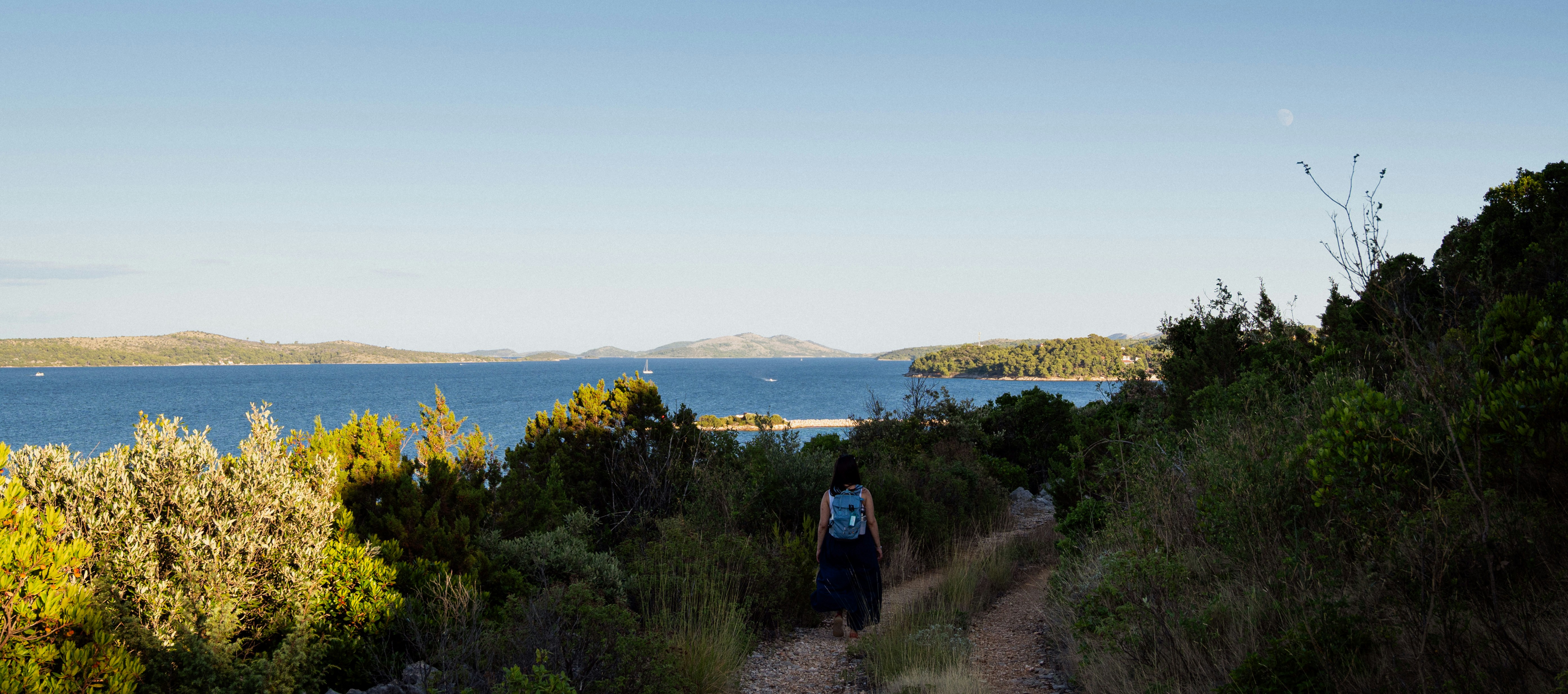 Woman walks on a path towards the ocean.