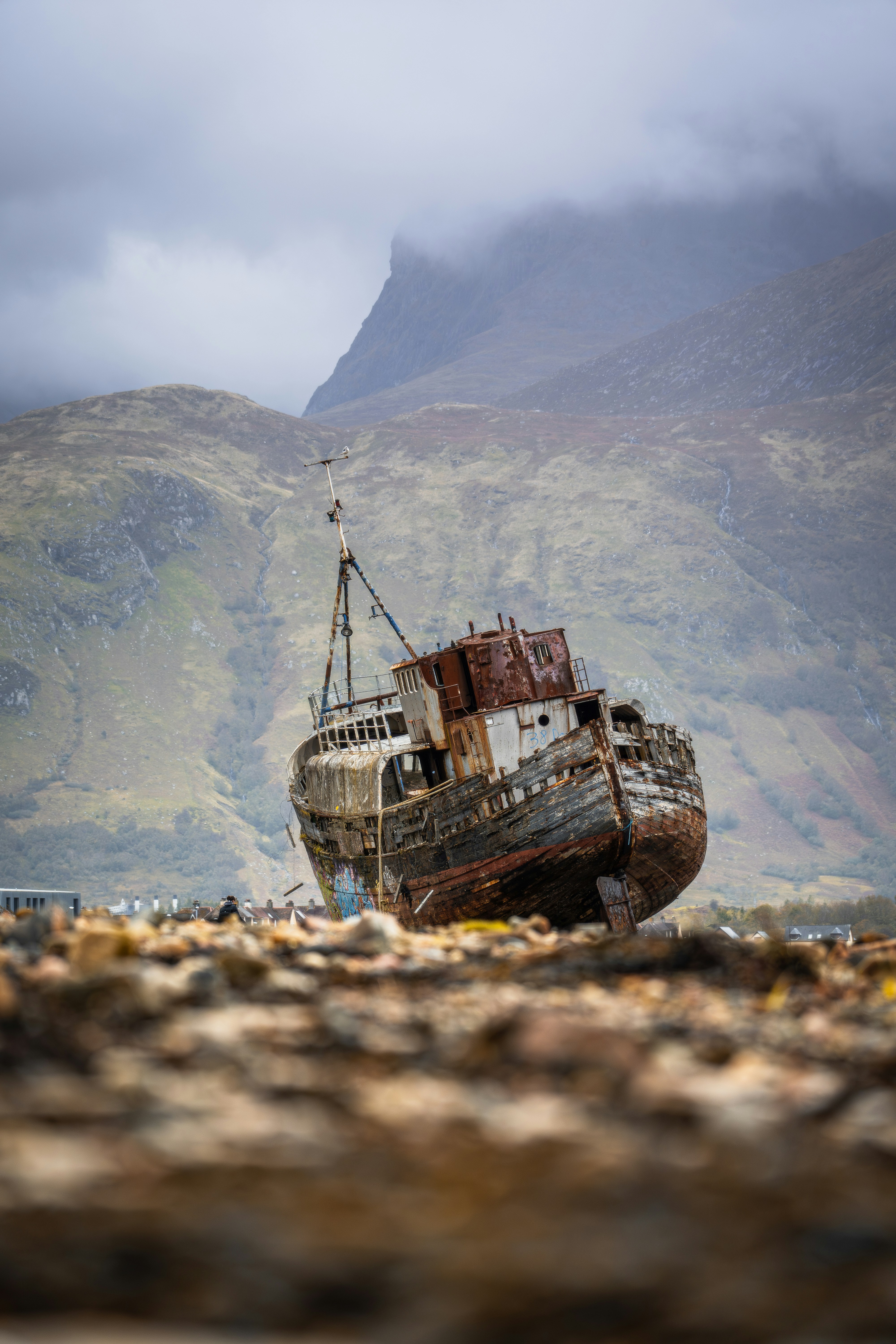Rusted shipwreck on a rocky shore with mountains behind