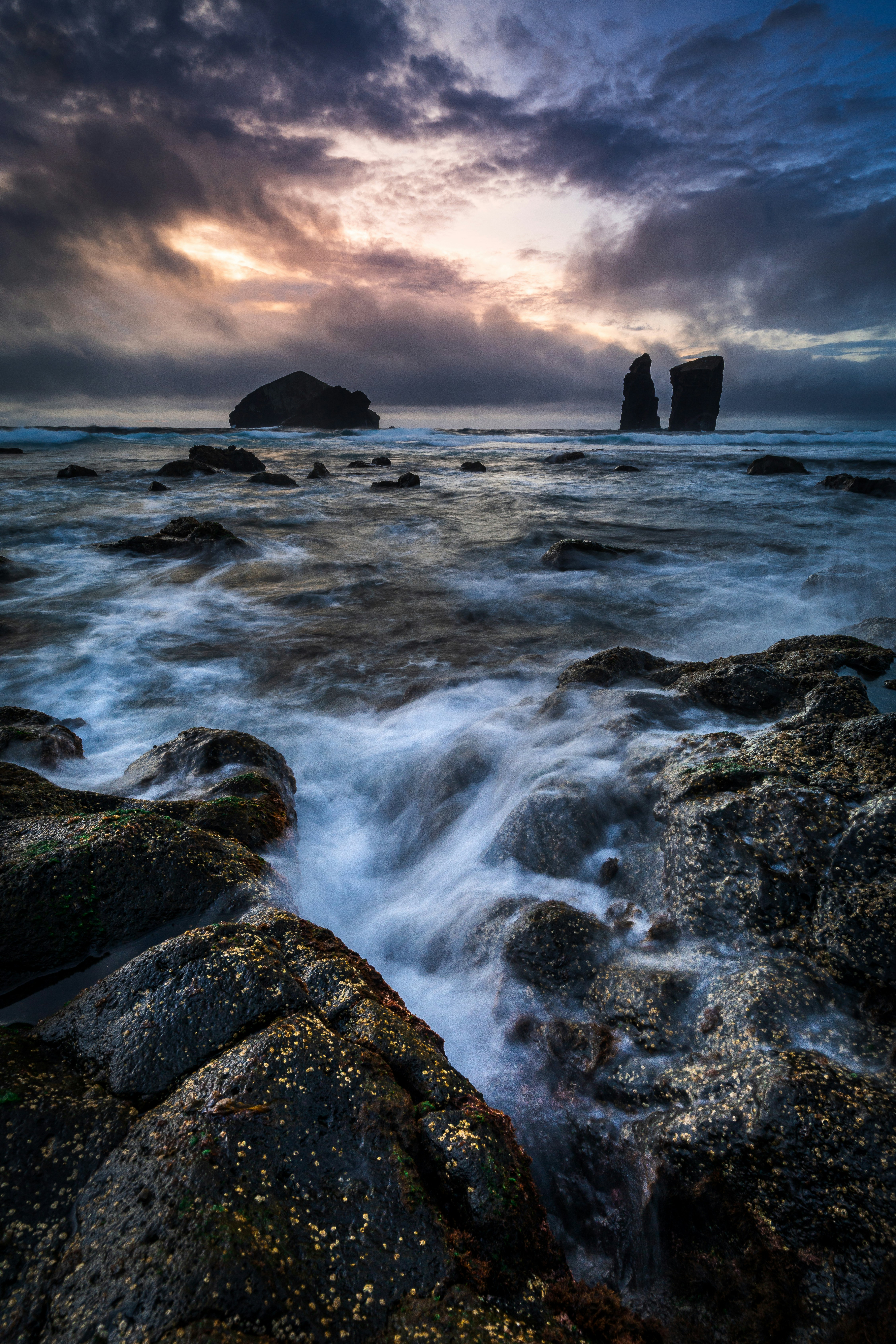Dramatic ocean waves crash against rocky shore at sunset
