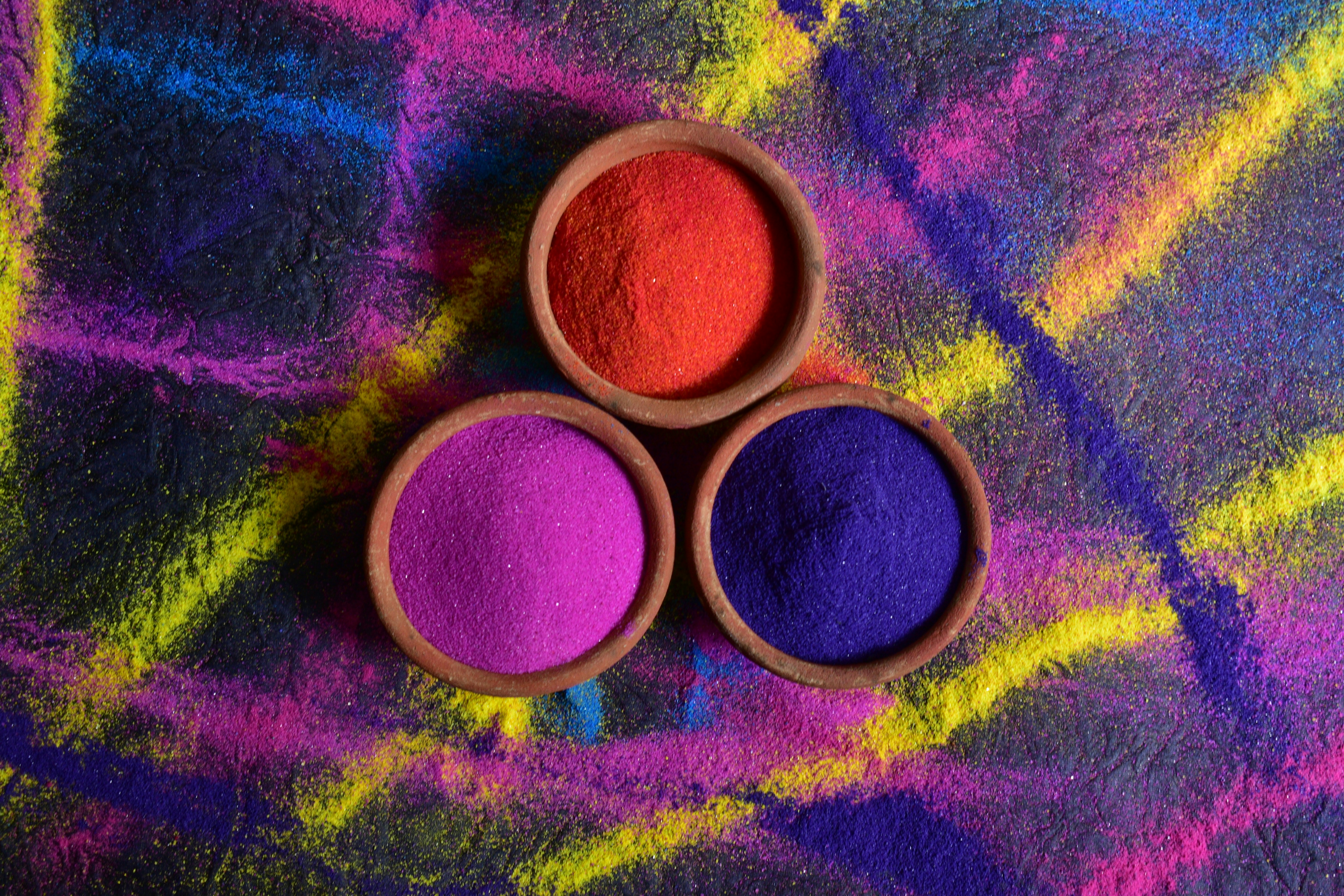 Three bowls of colorful powders on vibrant background