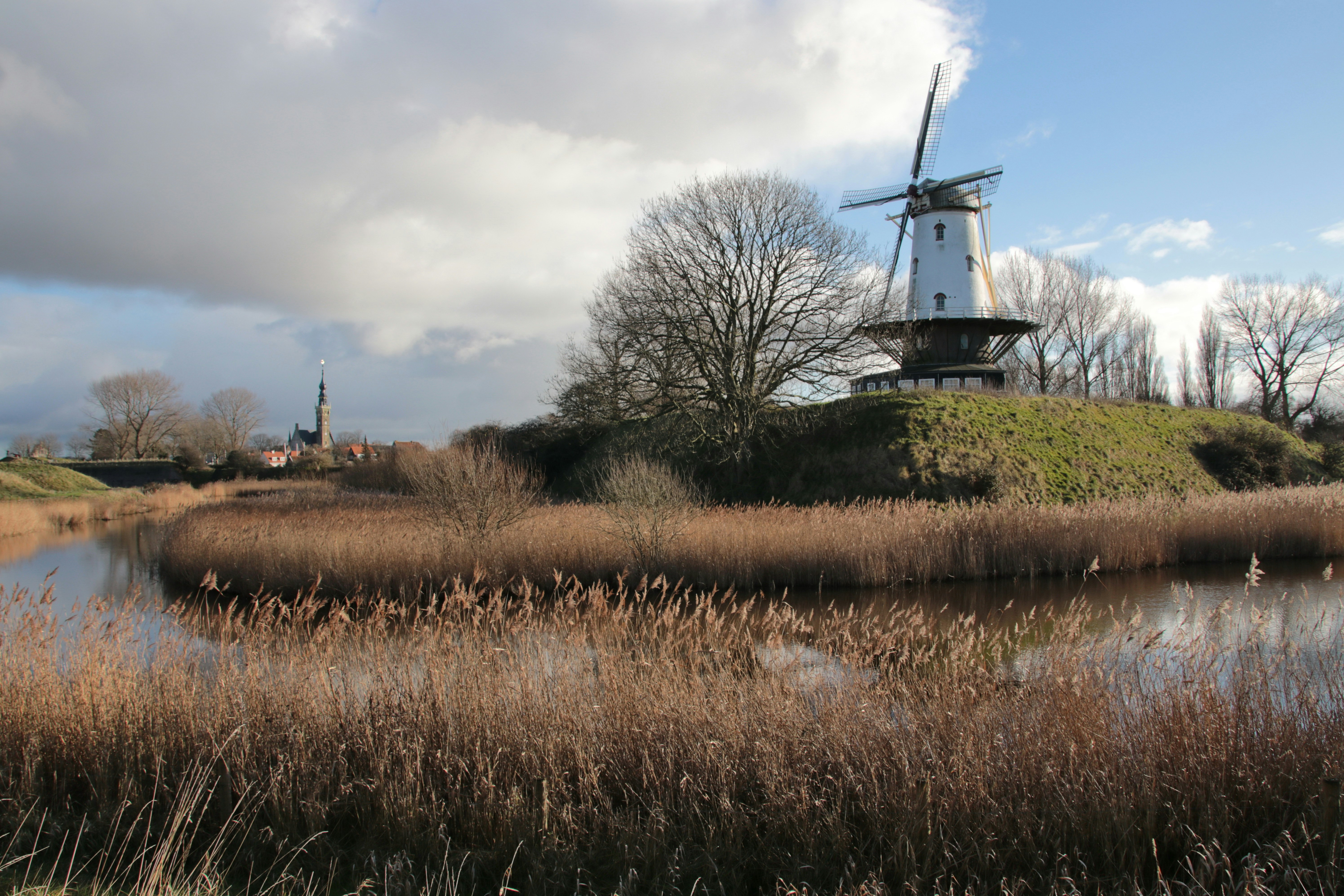White windmill on a grassy hill by a canal.