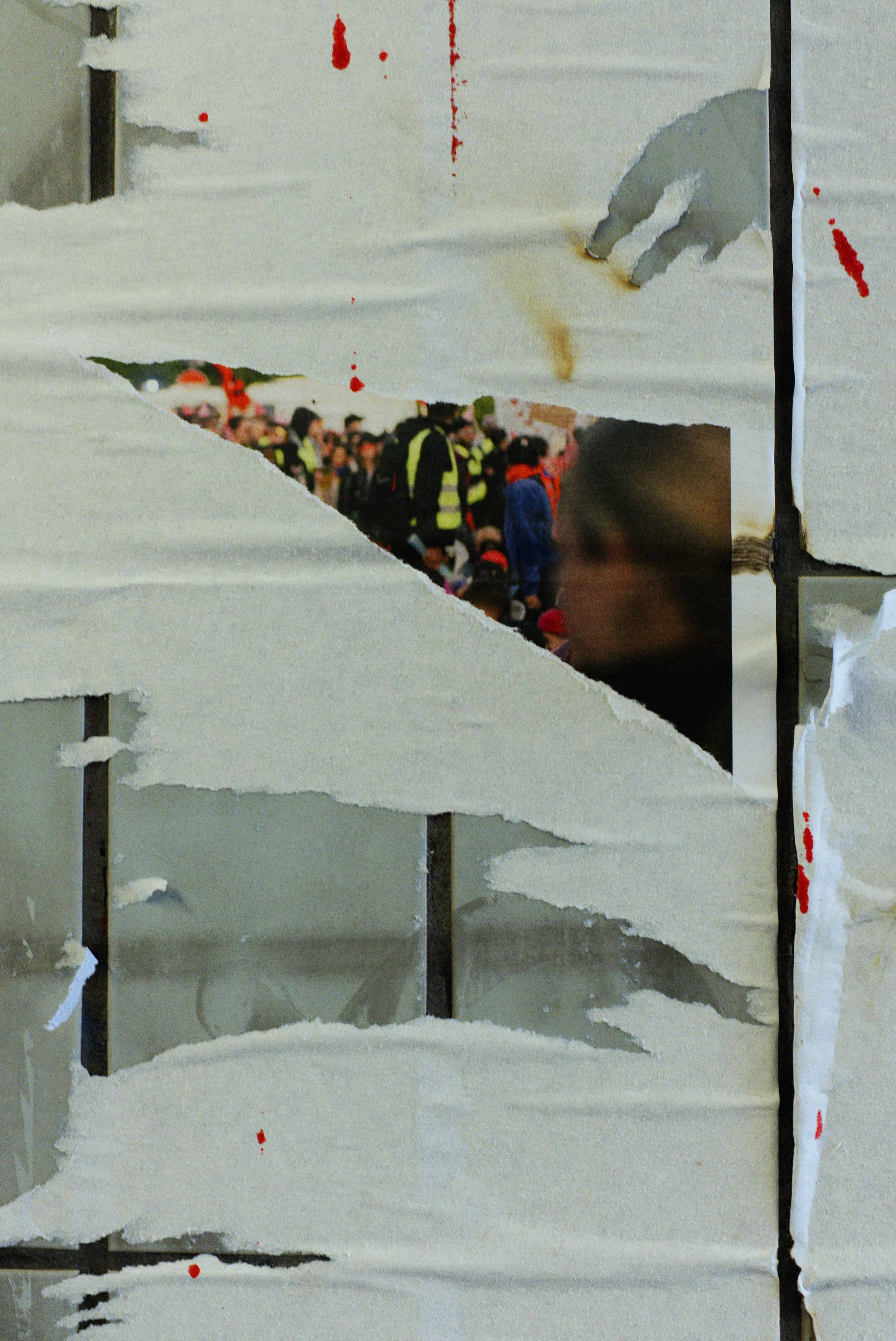 Torn posters reveal a crowd with people in high-visibility vests.