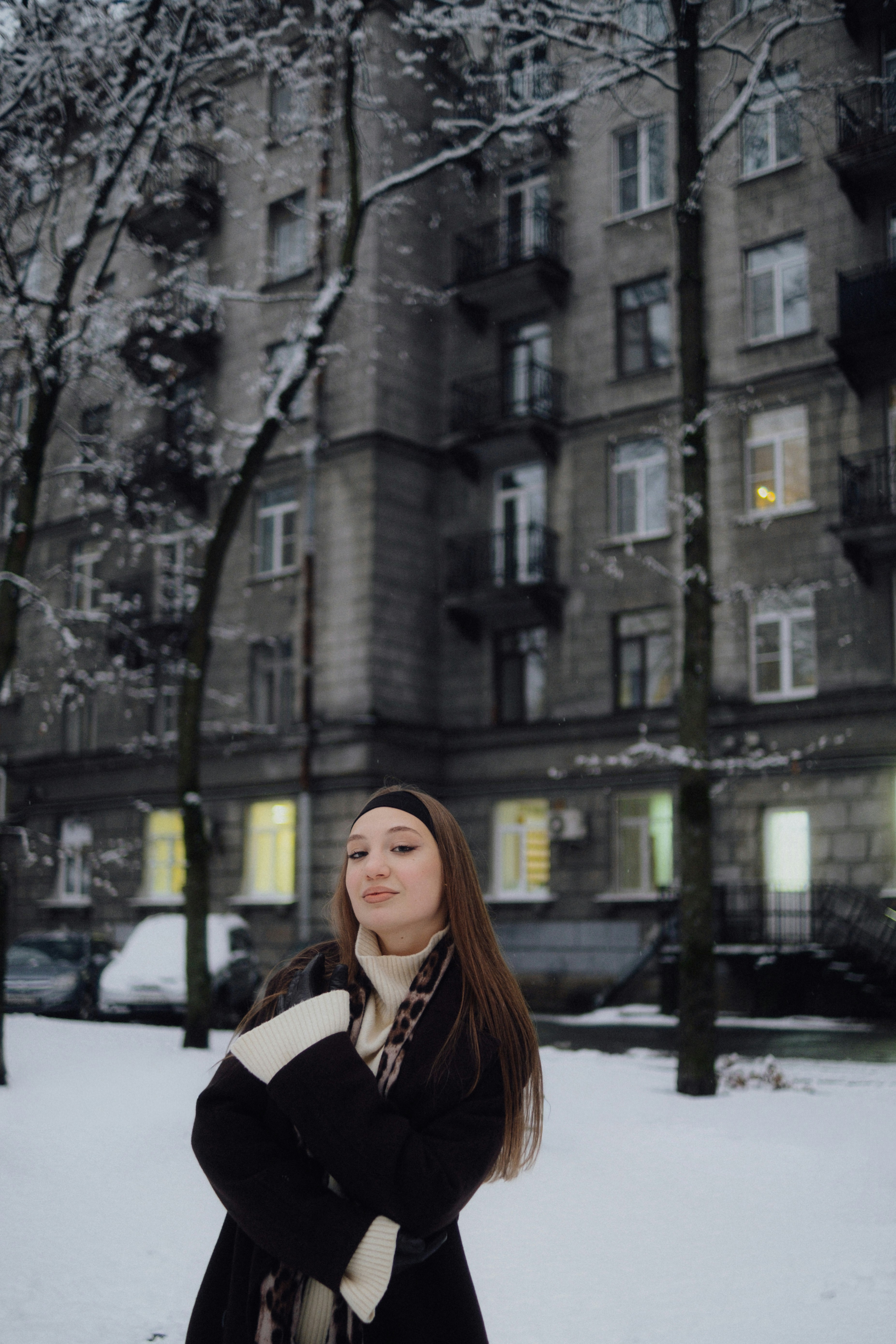 Young woman standing in snow near apartment building.