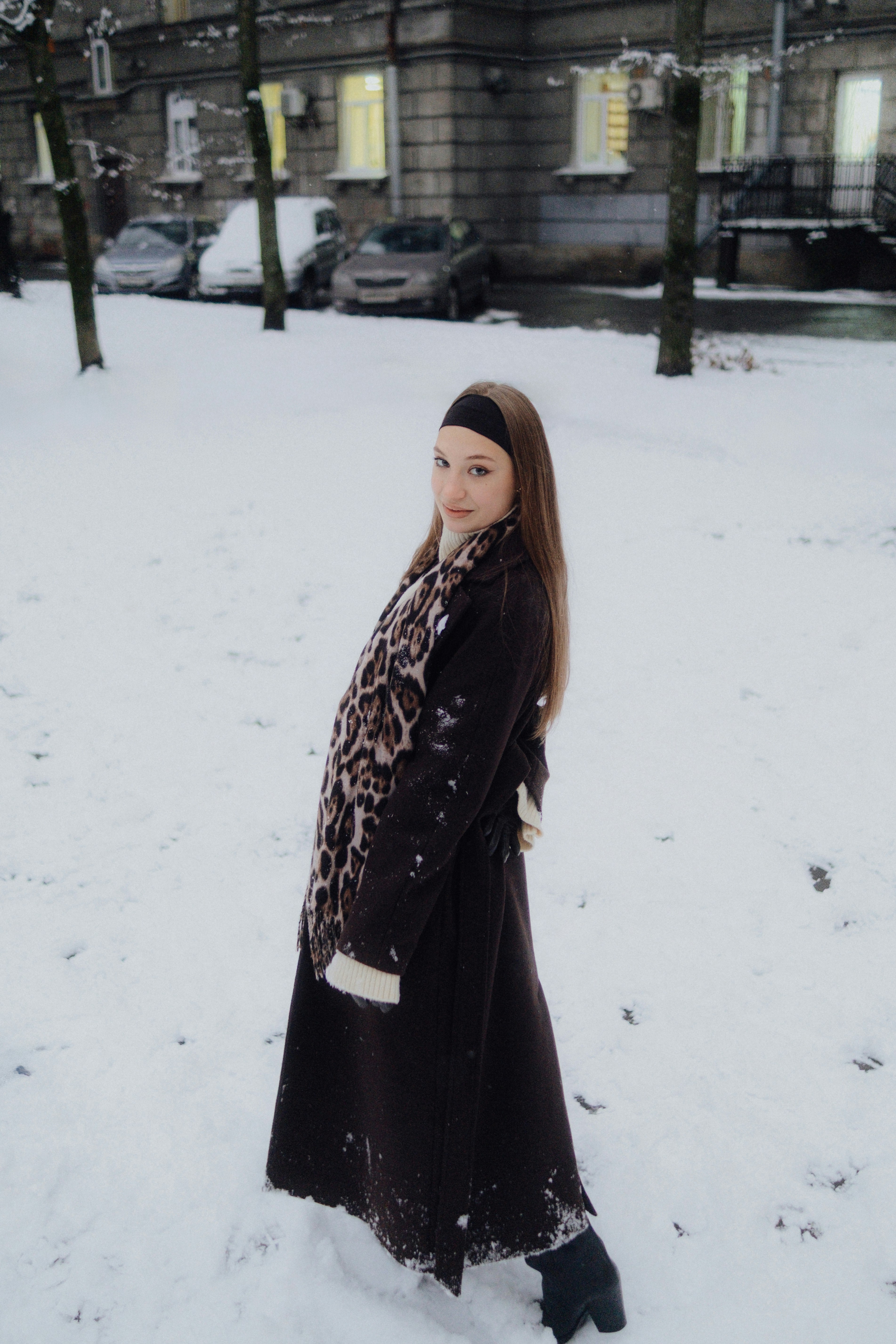 A young woman in a coat stands in the snow.