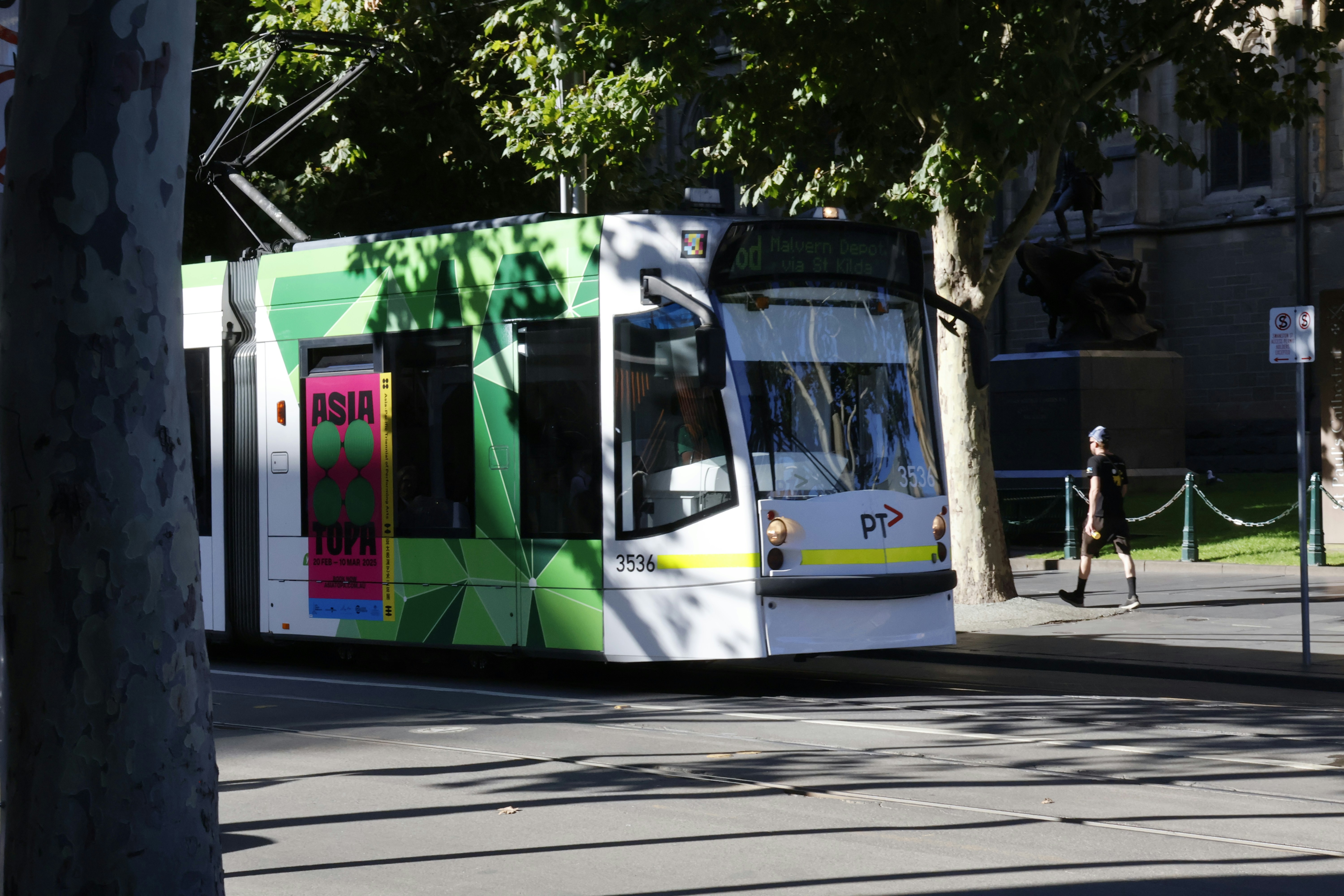 A tram with green accents drives down a street.