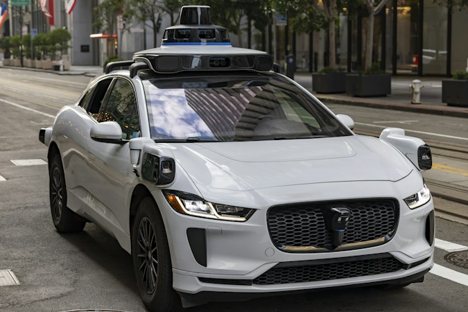 A white autonomous vehicle with roof-mounted sensors driving on a city street