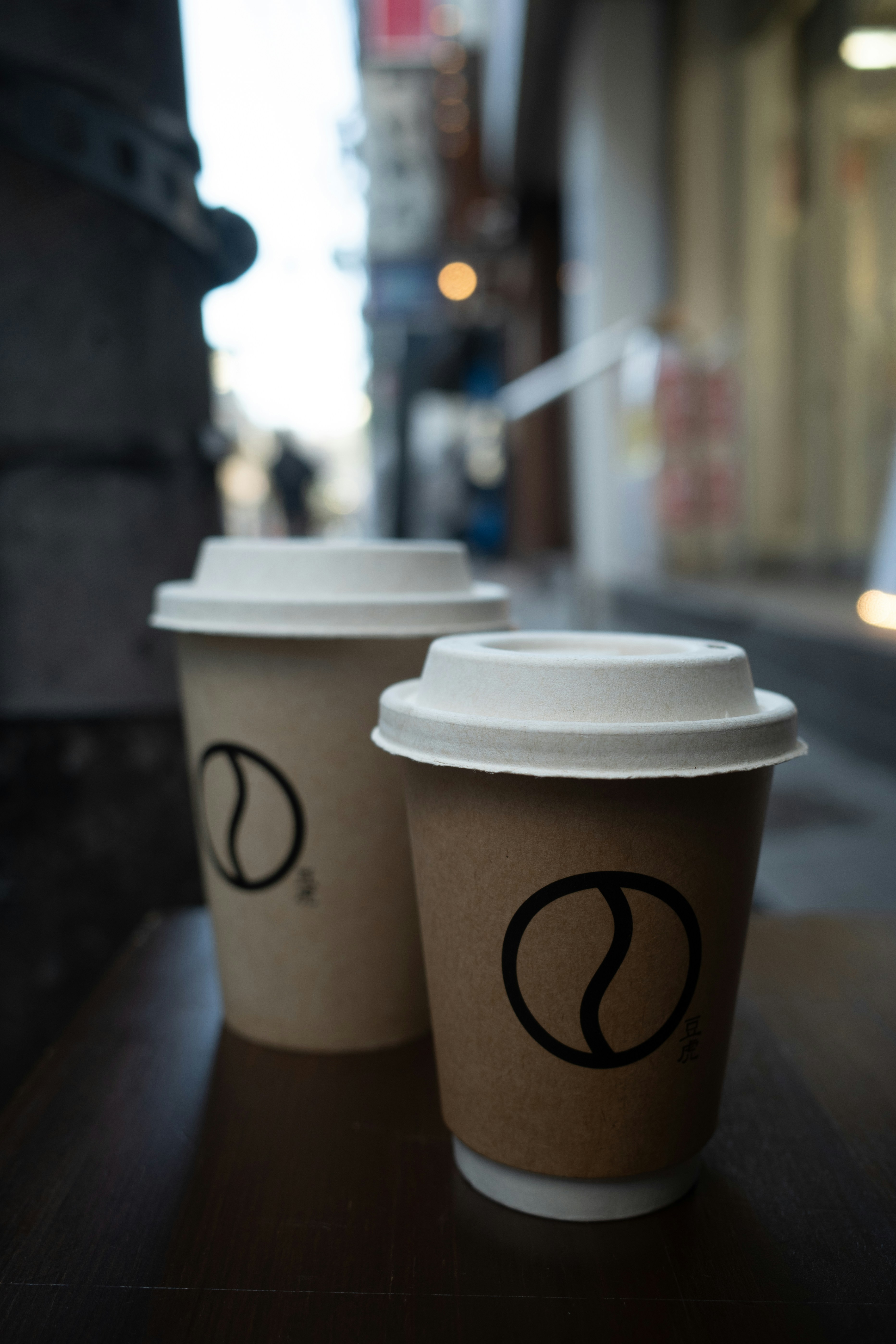 Two disposable coffee cups with lids on a table