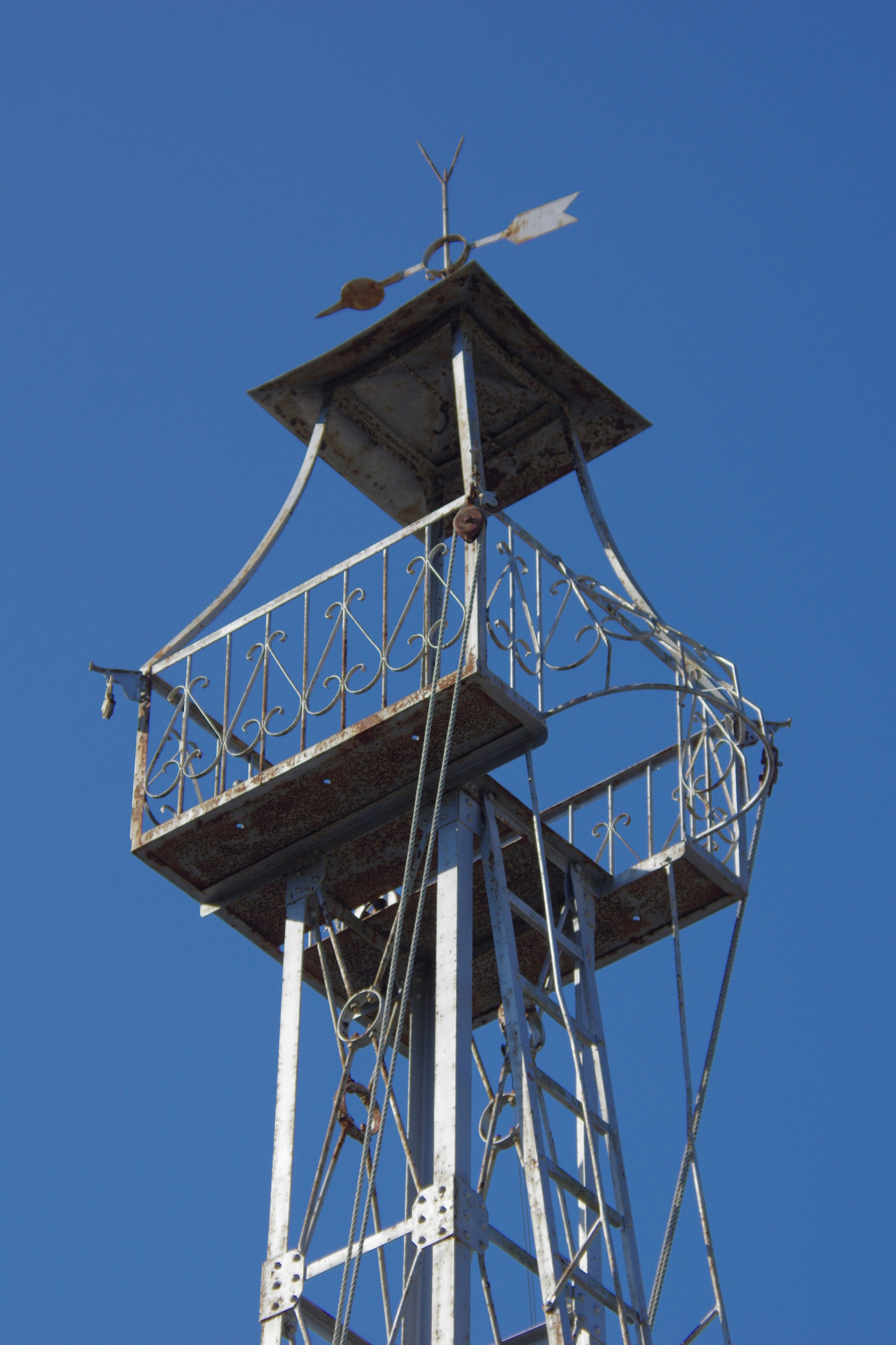 Weather vane atop a rustic metal tower against blue sky