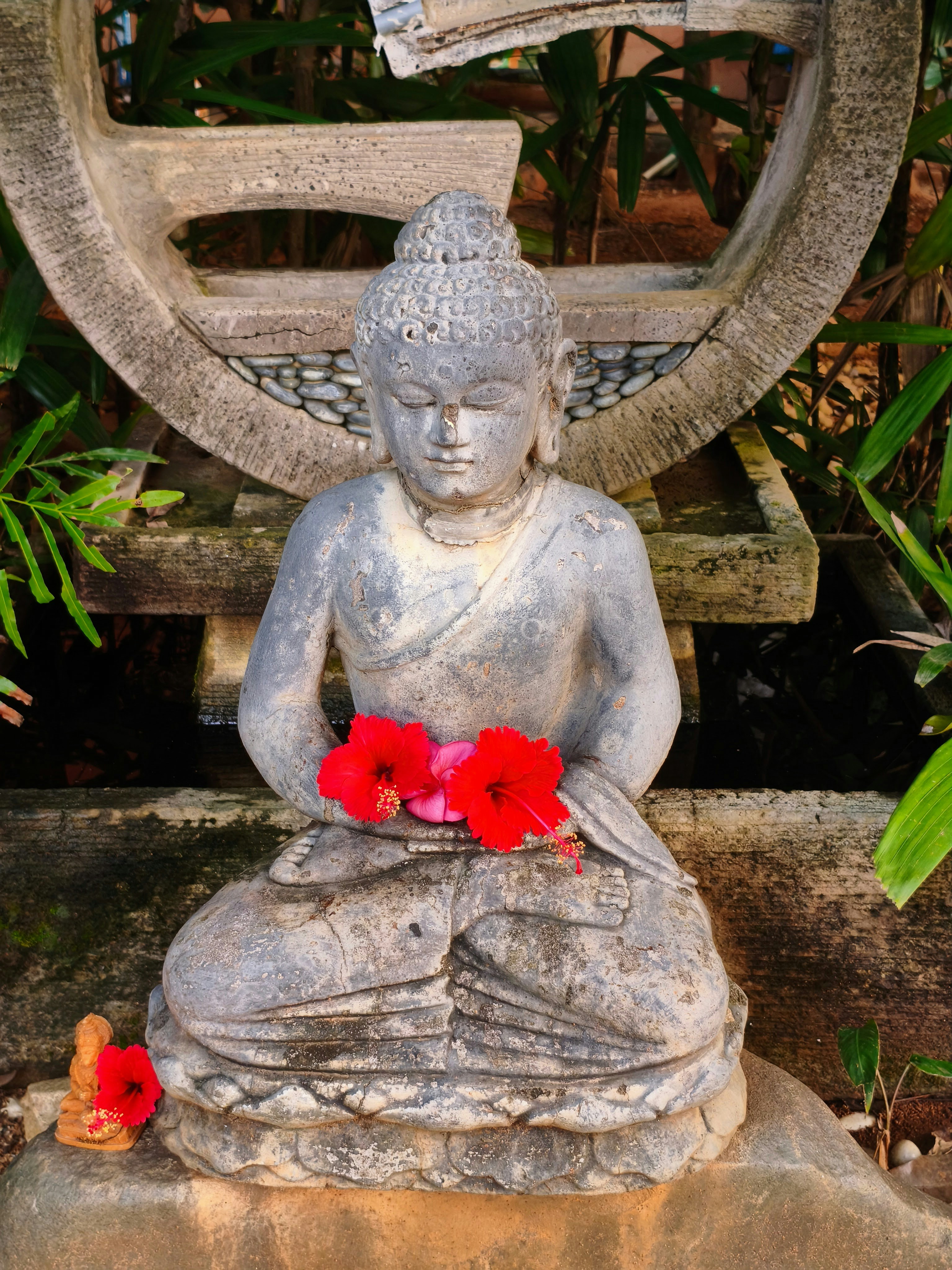 Steinerne Buddha-Statue mit roten Blumen im Garten