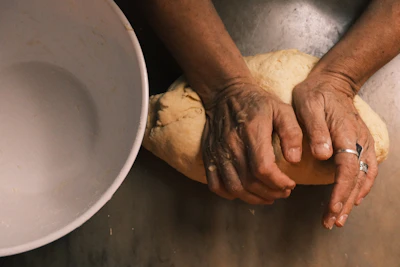Hands kneading dough next to a white bowl