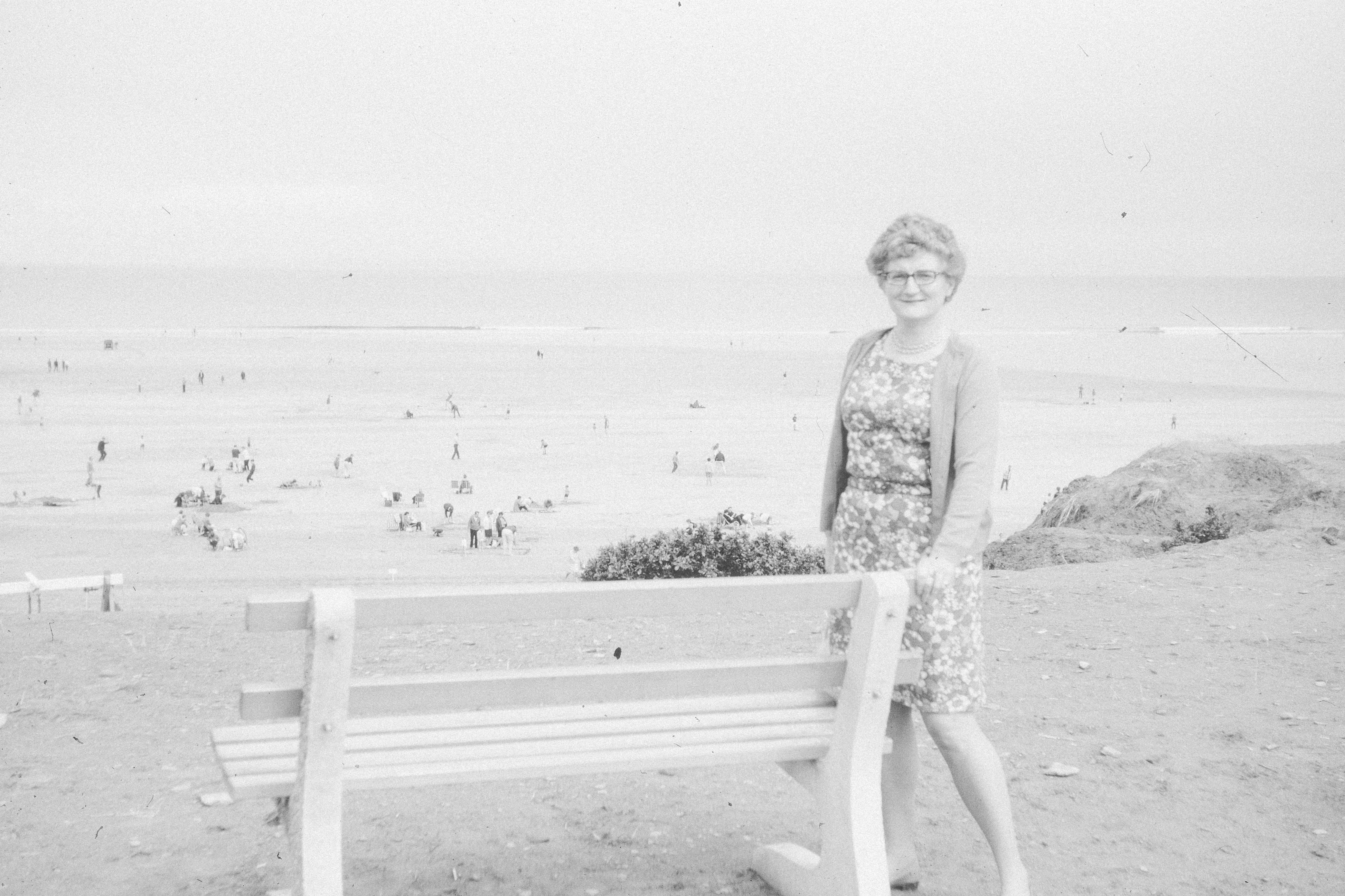 Woman standing by a bench overlooking a crowded beach.