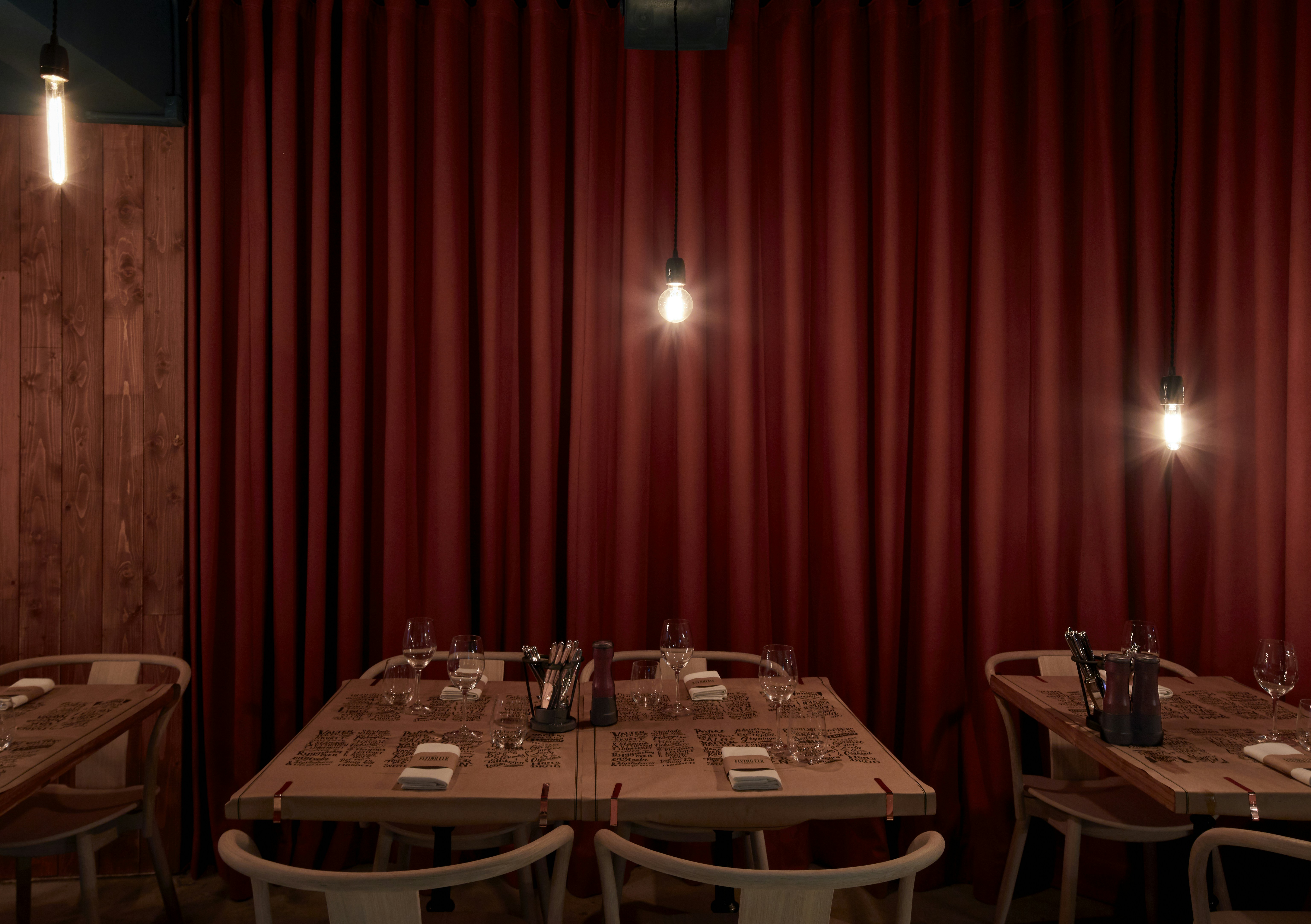 Restaurant tables set with place settings and red curtains