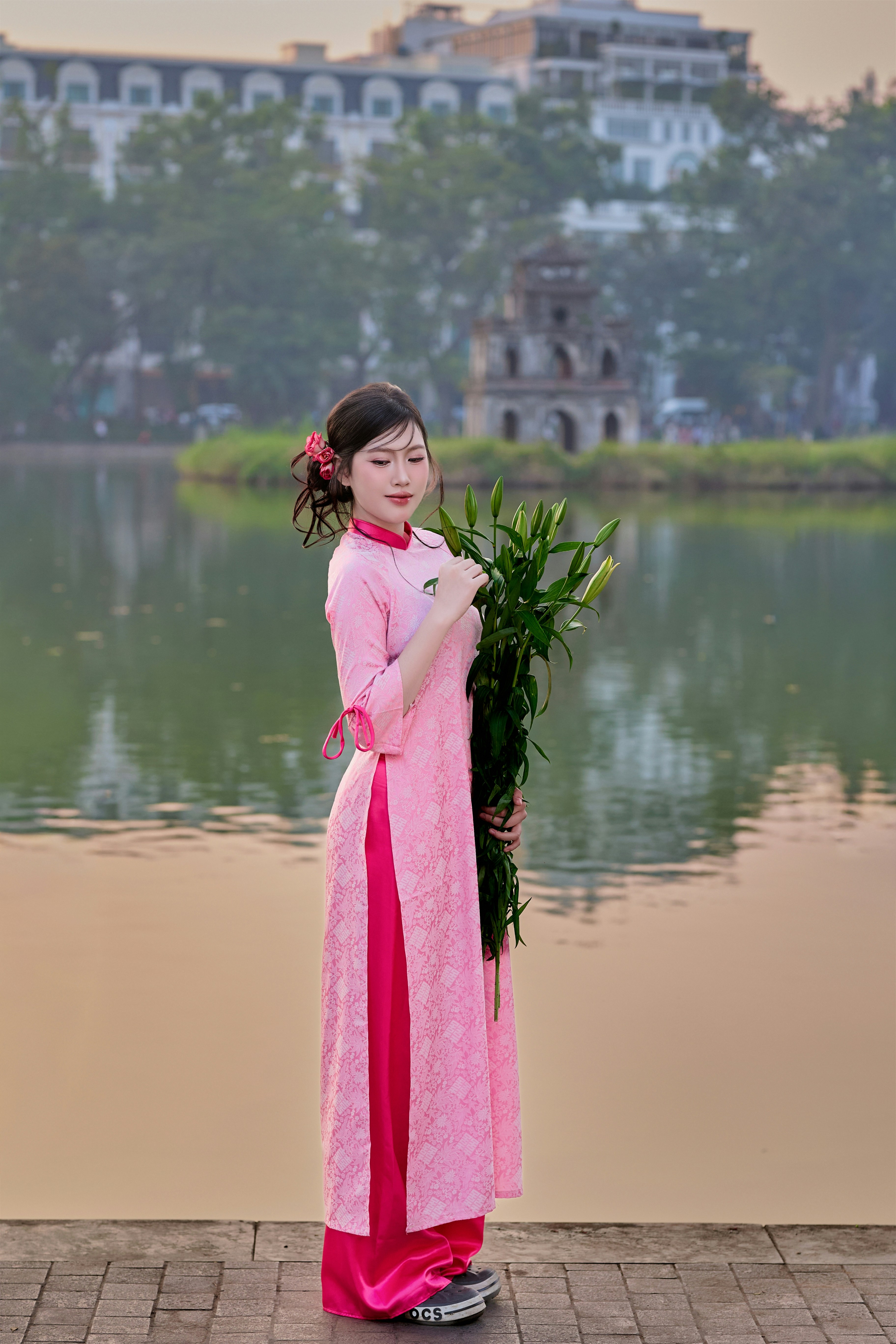 Young woman in pink ao dai holding flowers by lake