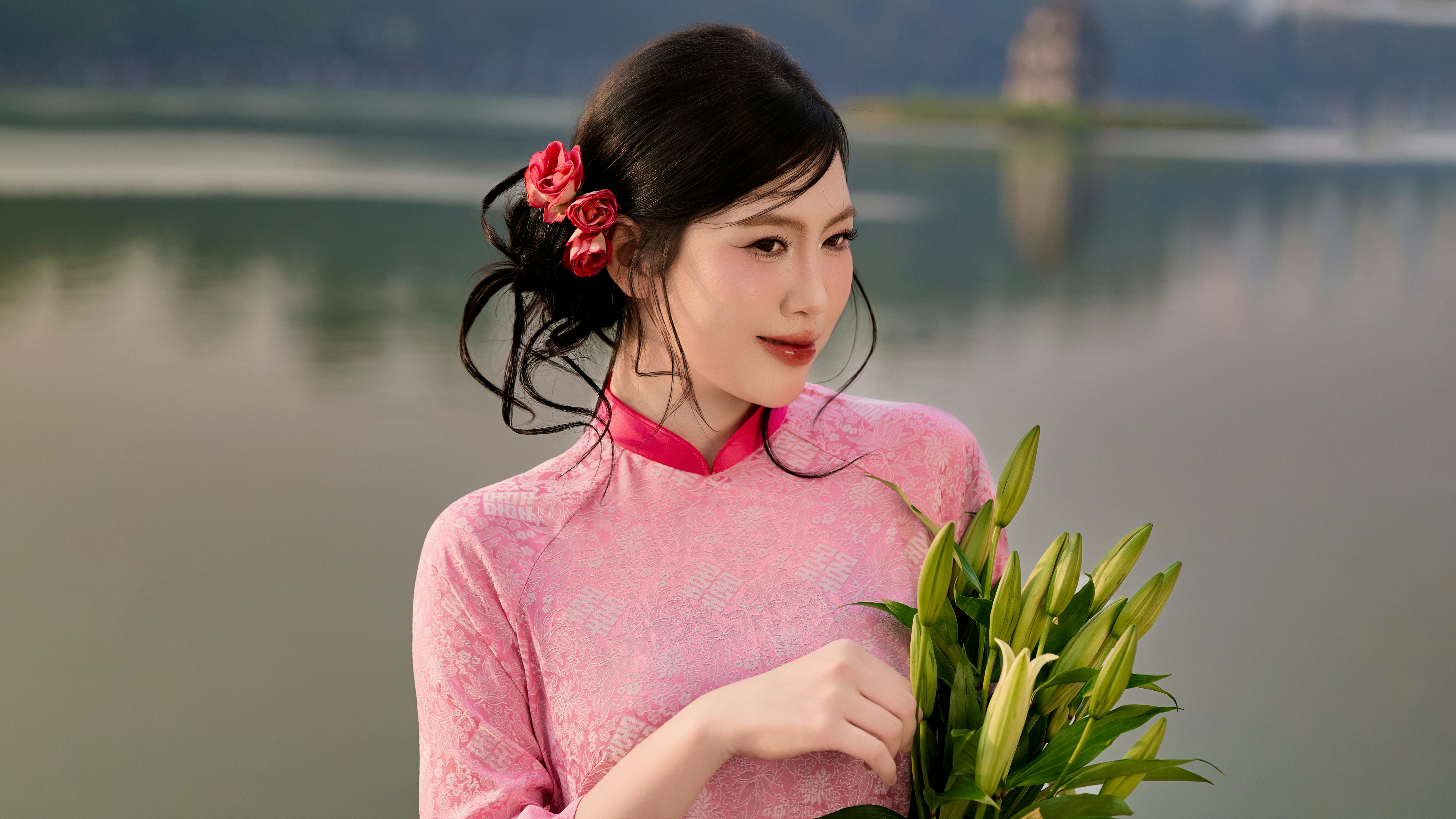 Woman in pink dress holding lilies by a lake