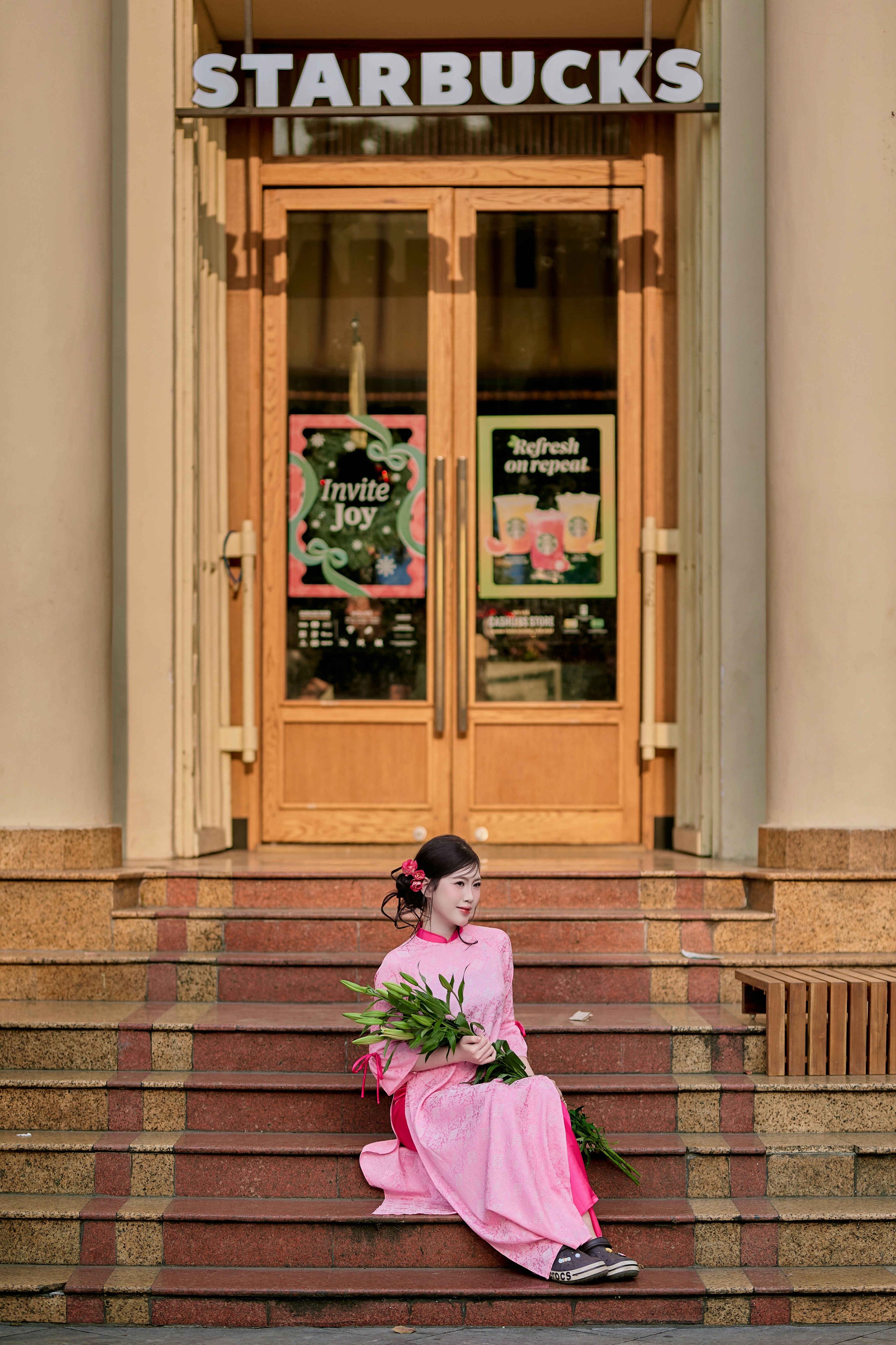 Woman in pink dress sits on starbucks steps with flowers