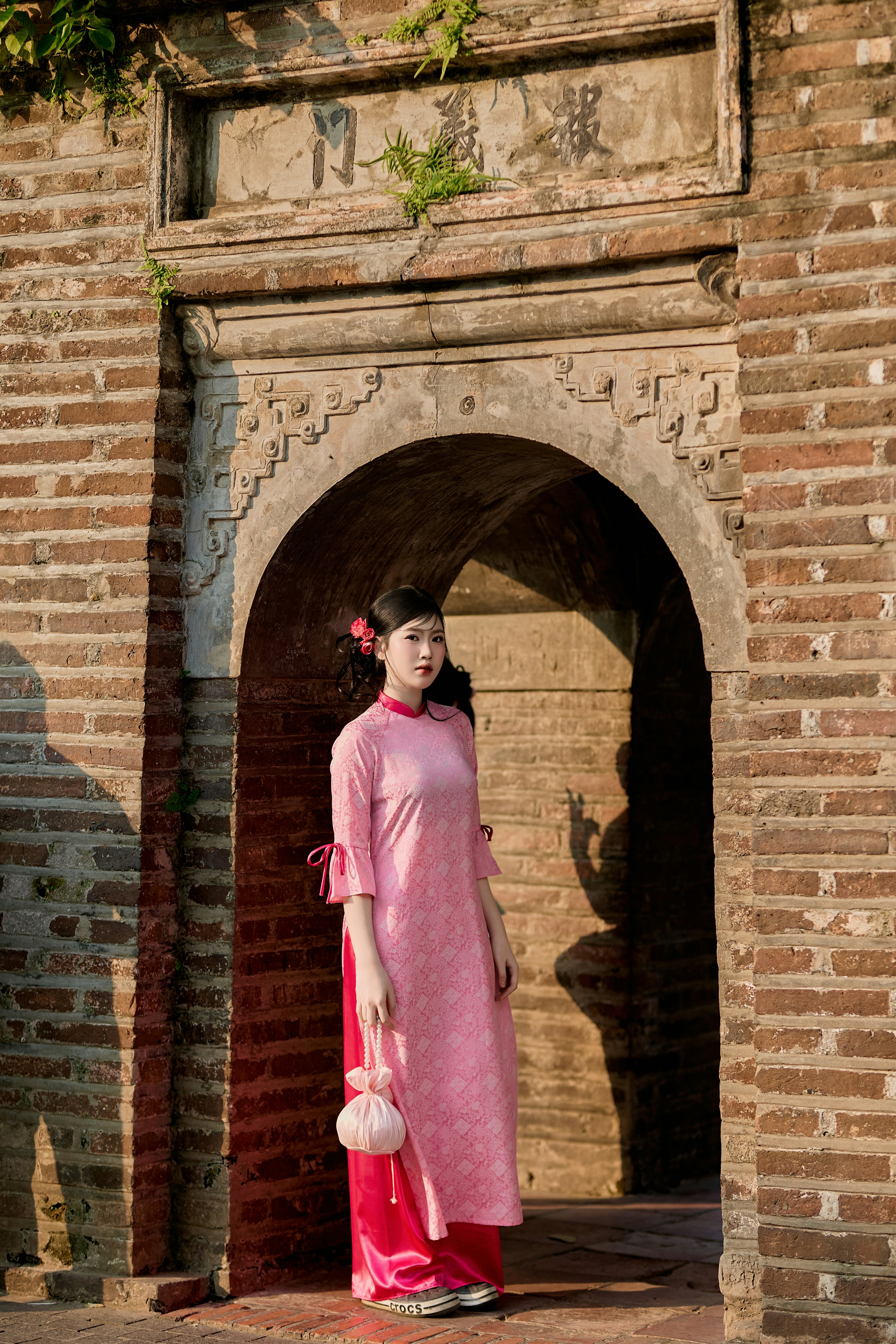 Woman in pink traditional dress stands in an archway.