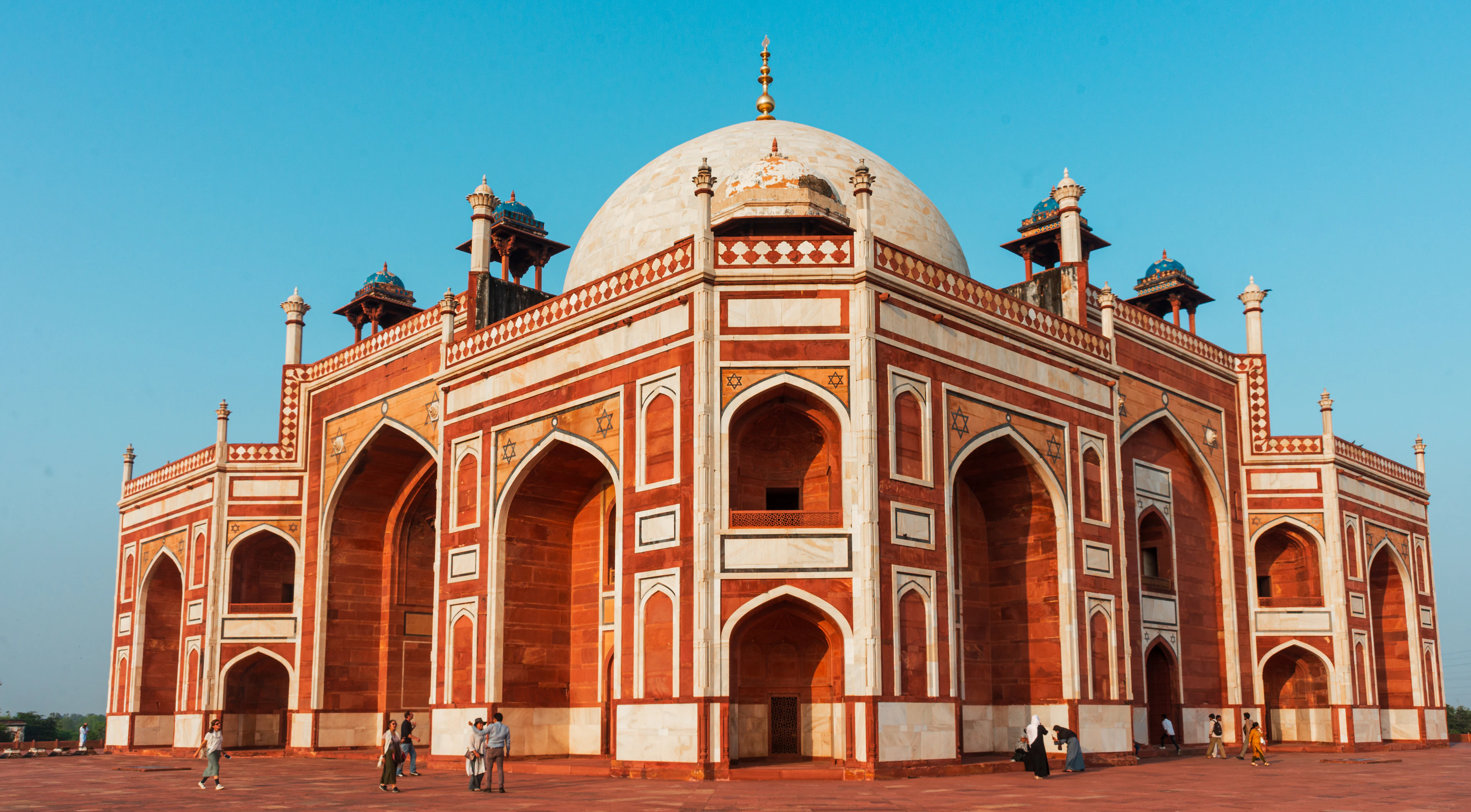 Humayun's Tomb's red sandstone and white marble facade under a clear blue sky, visitors walking in front.