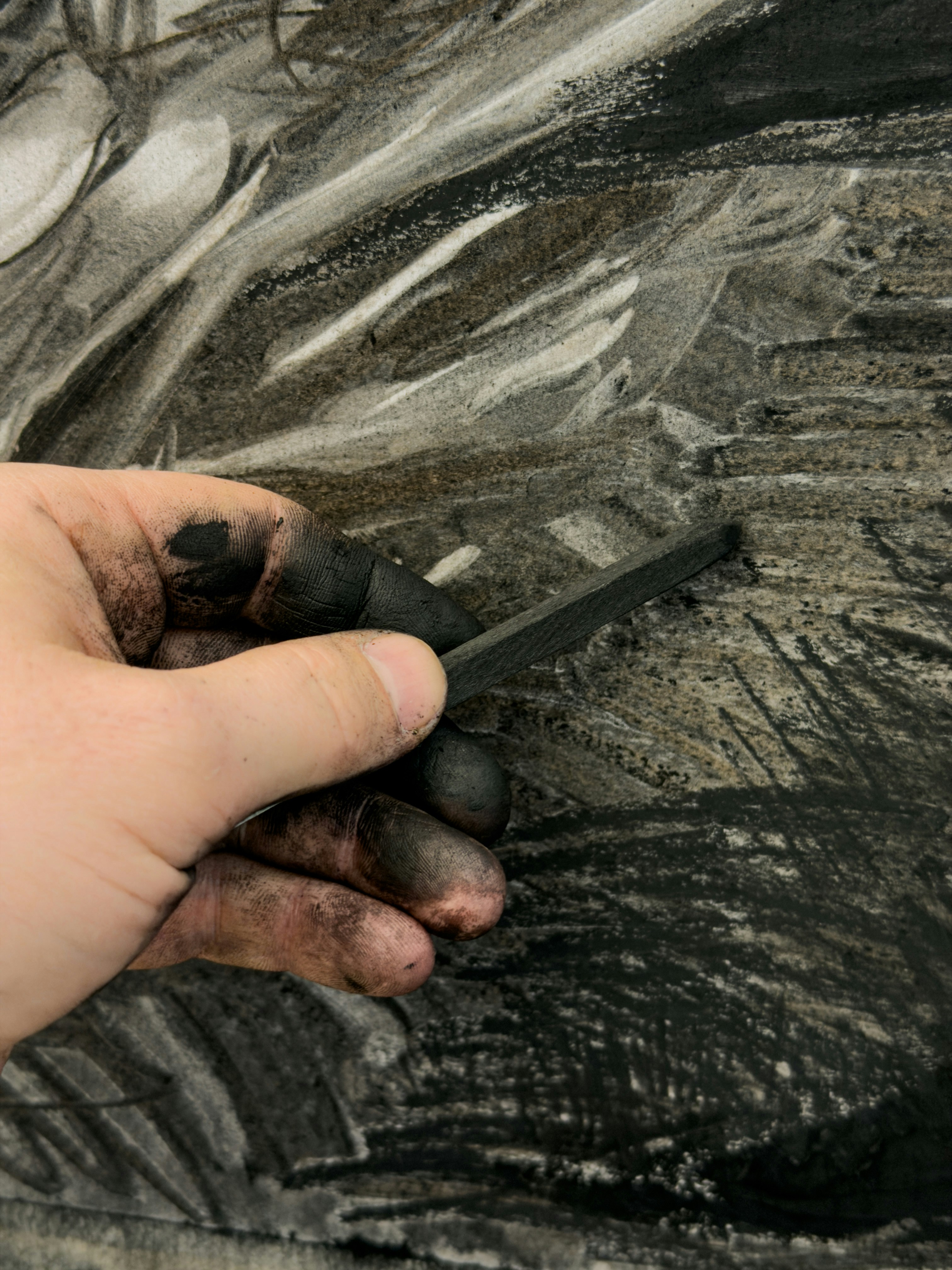 Artist's hand holding charcoal over drawing