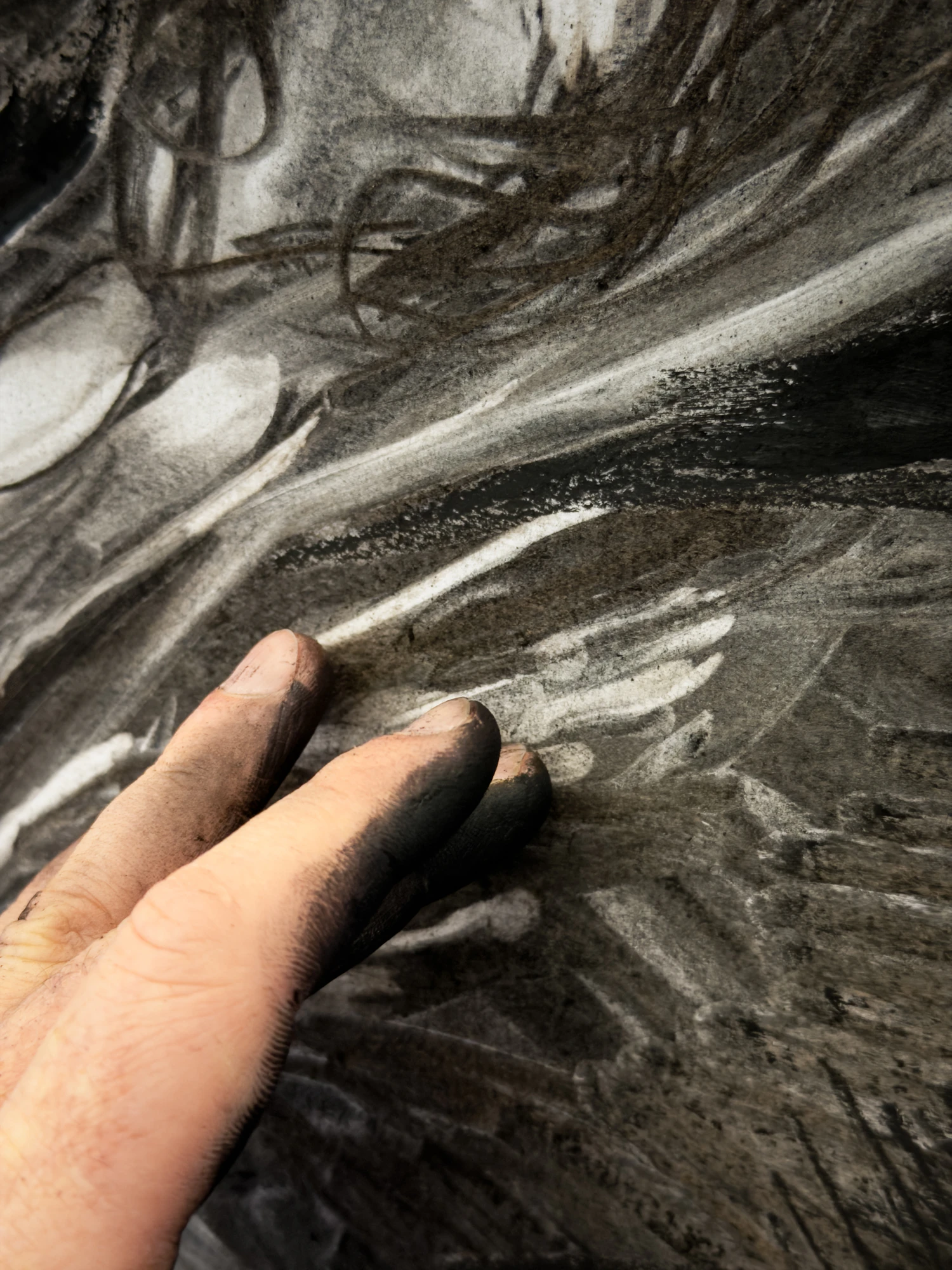 A hand drawing a charcoal line across a large sheet of paper