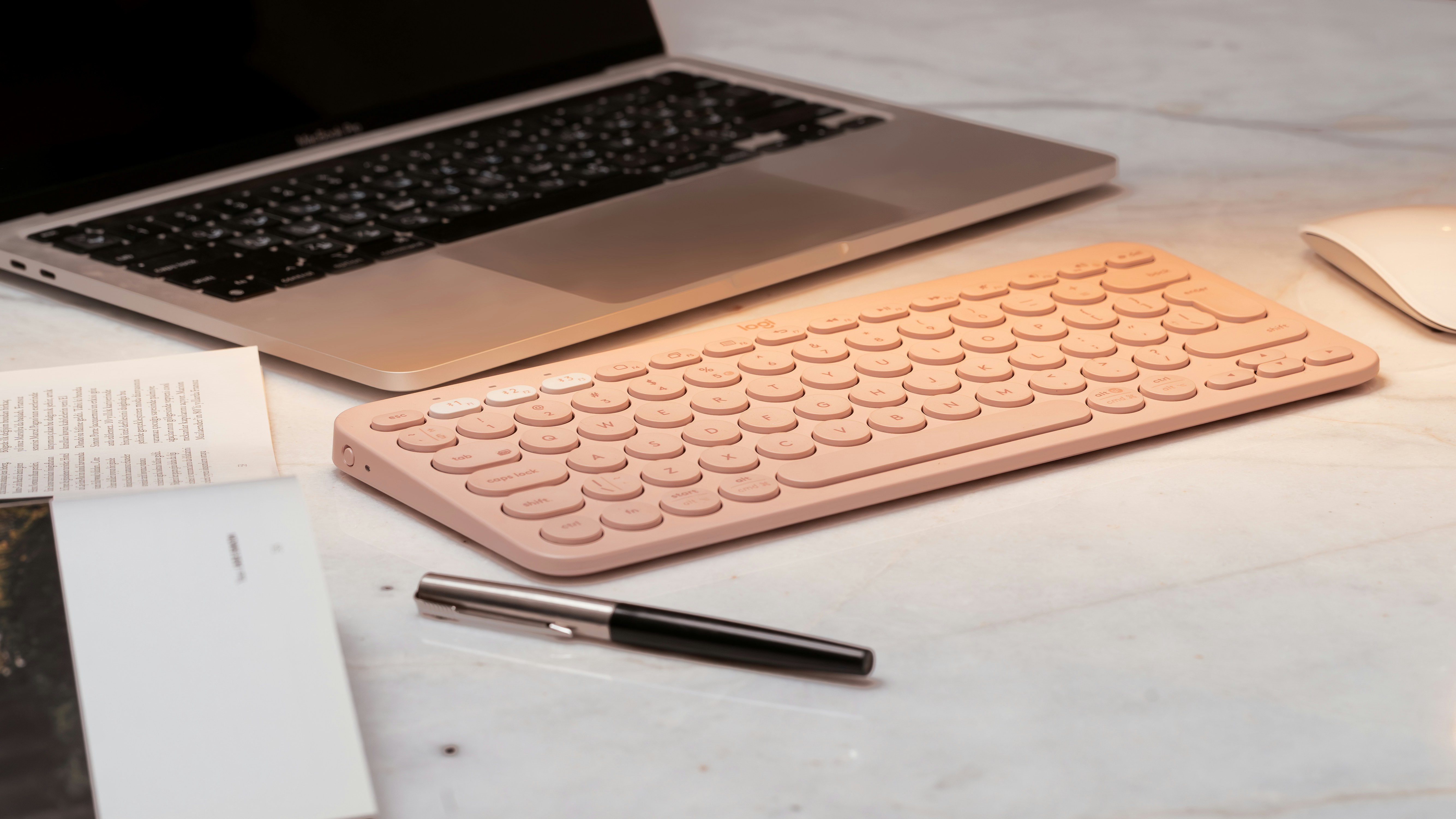 Pink keyboard and laptop on a desk.