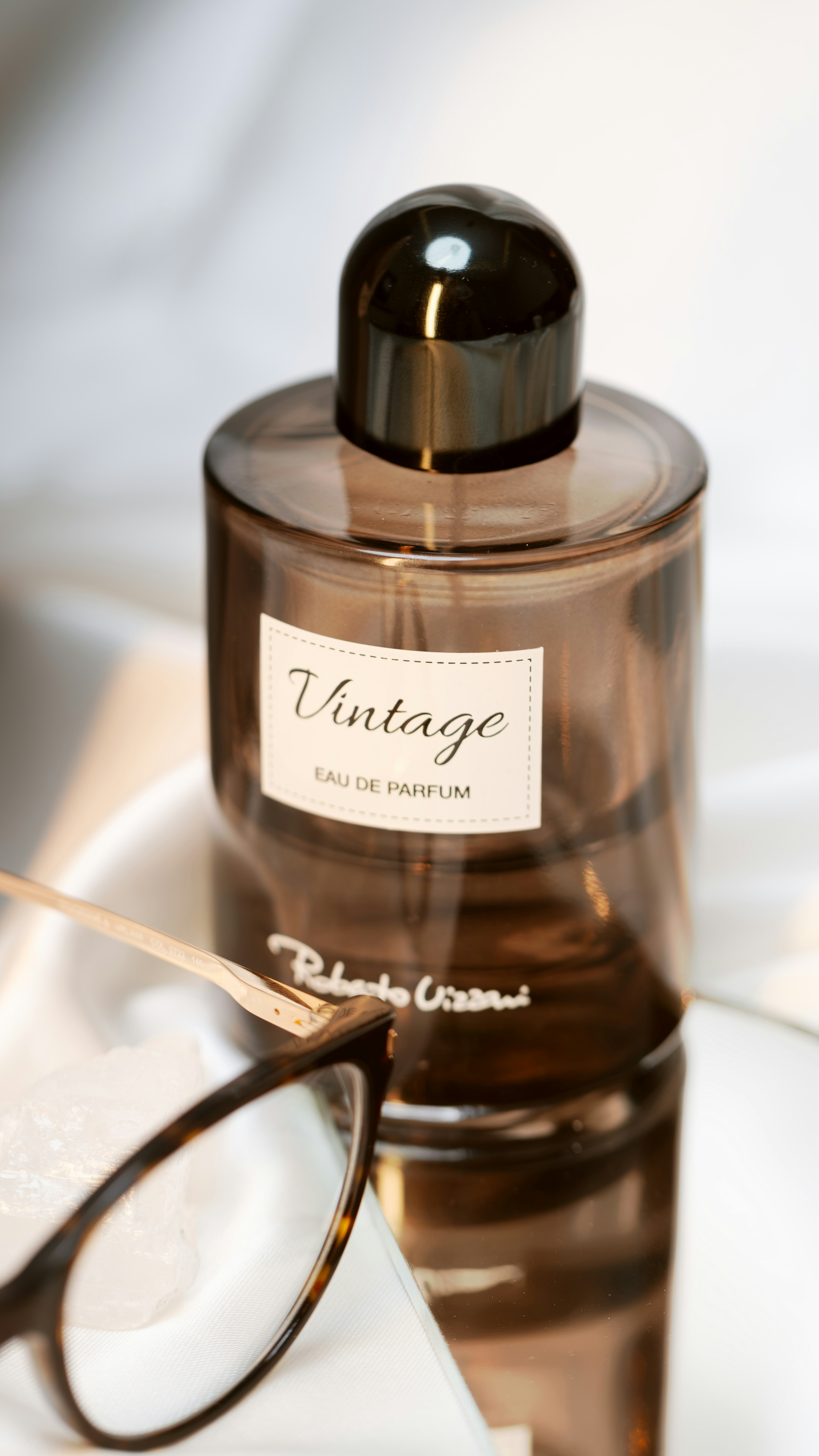 A vintage perfume bottle with glasses on a reflective surface.