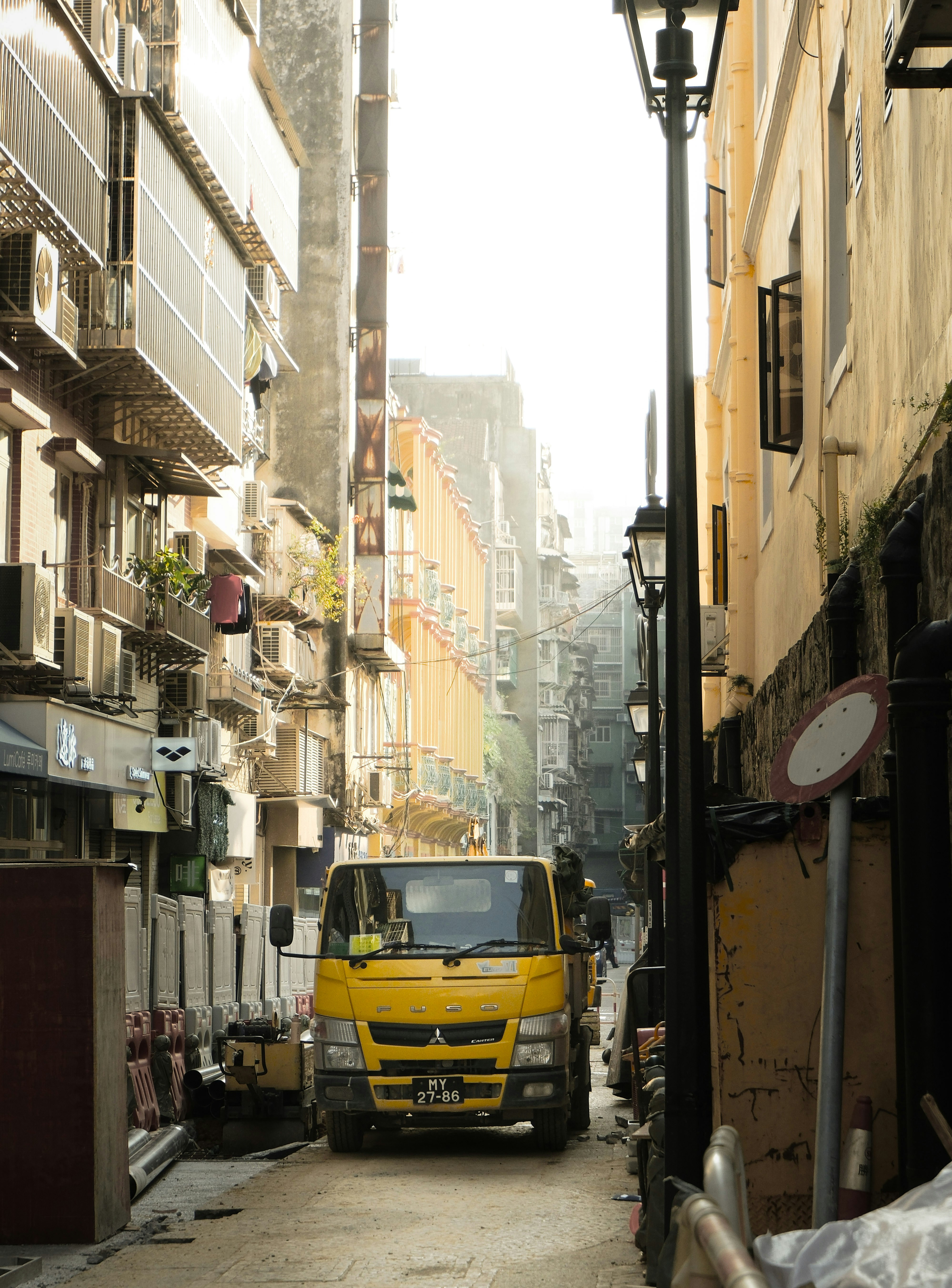 Yellow truck parked in a narrow city alleyway.