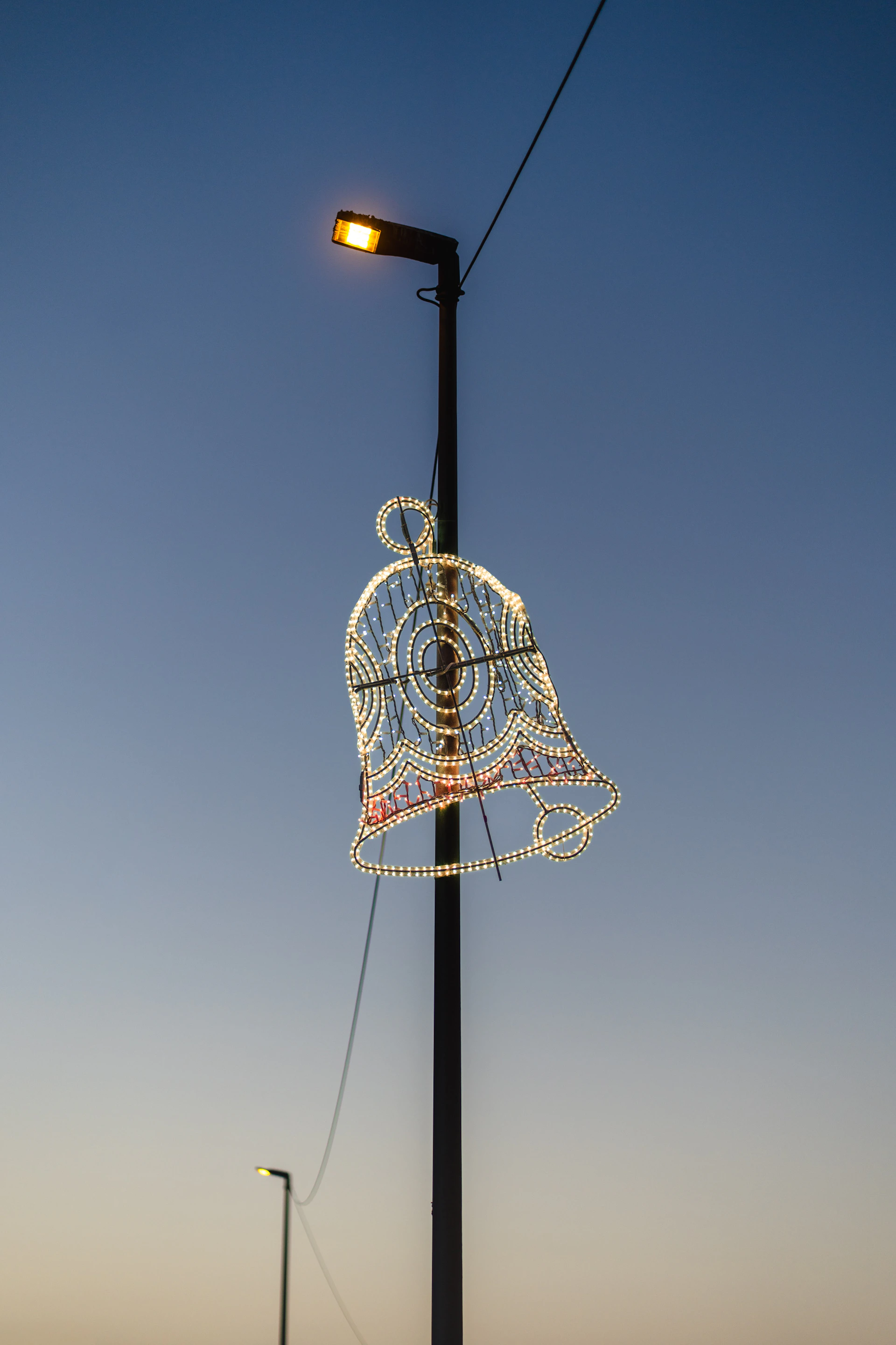 A decorative bell light hangs from a lamppost at dusk