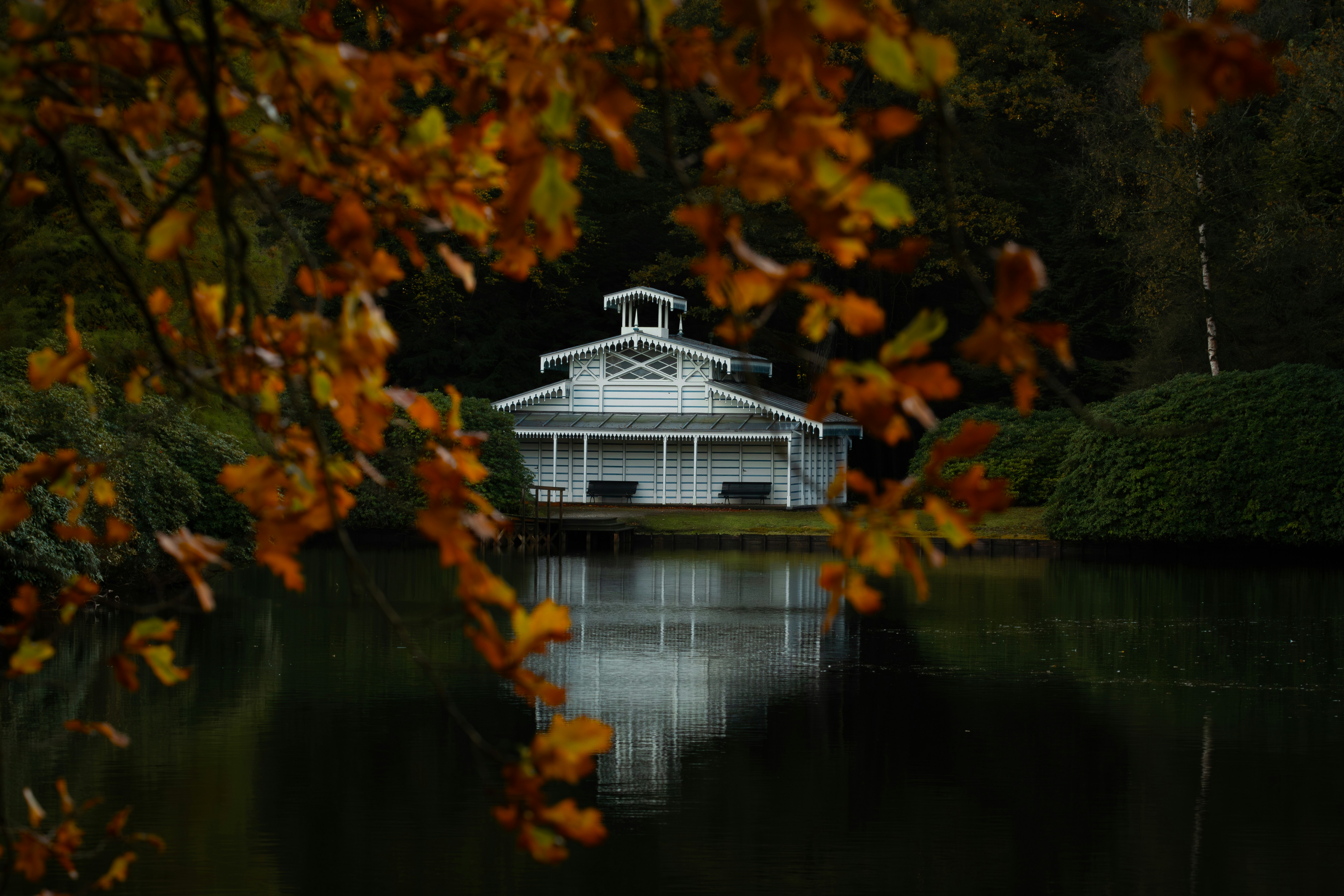 White boathouse reflected in calm water during autumn.