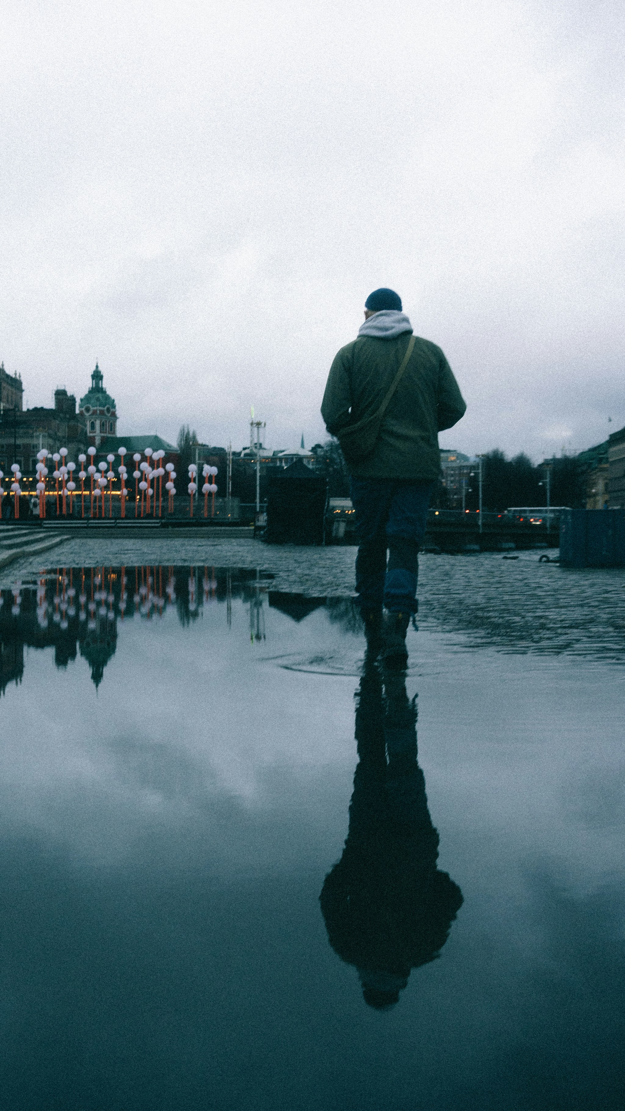 Man walking in puddles with reflection of city buildings reflected