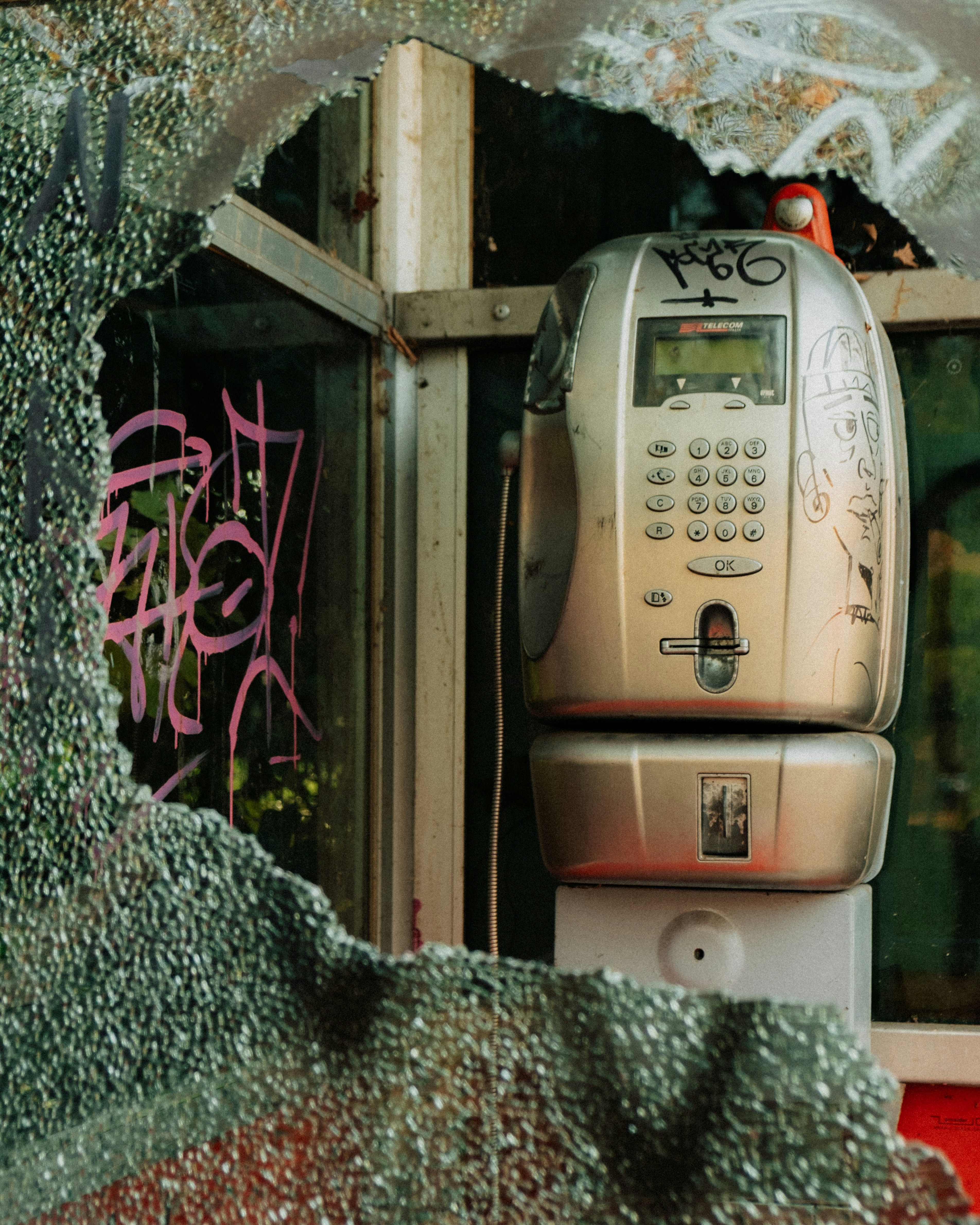 Graffiti-covered payphone inside broken booth
