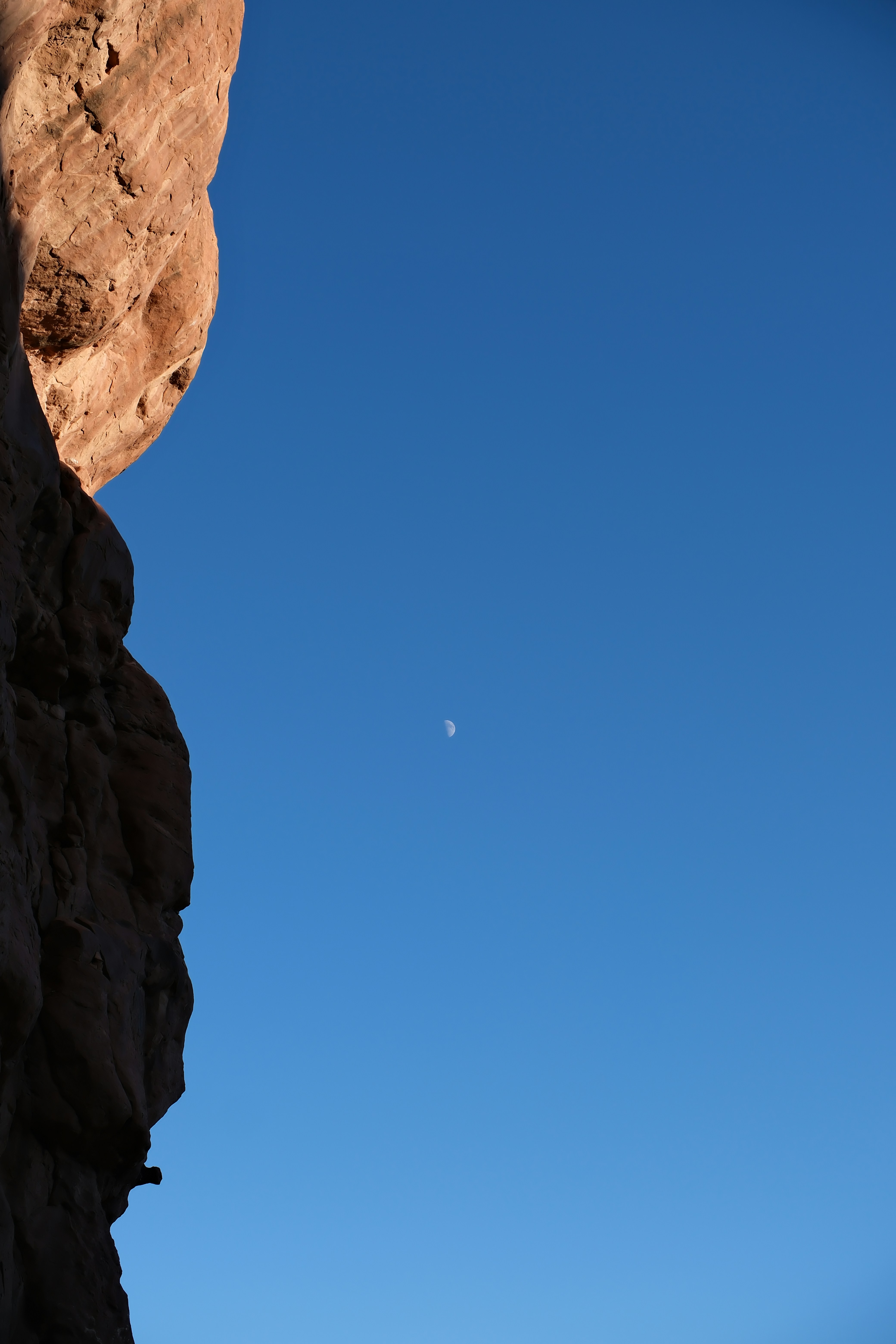 Crescent moon in a clear blue sky over rock formation