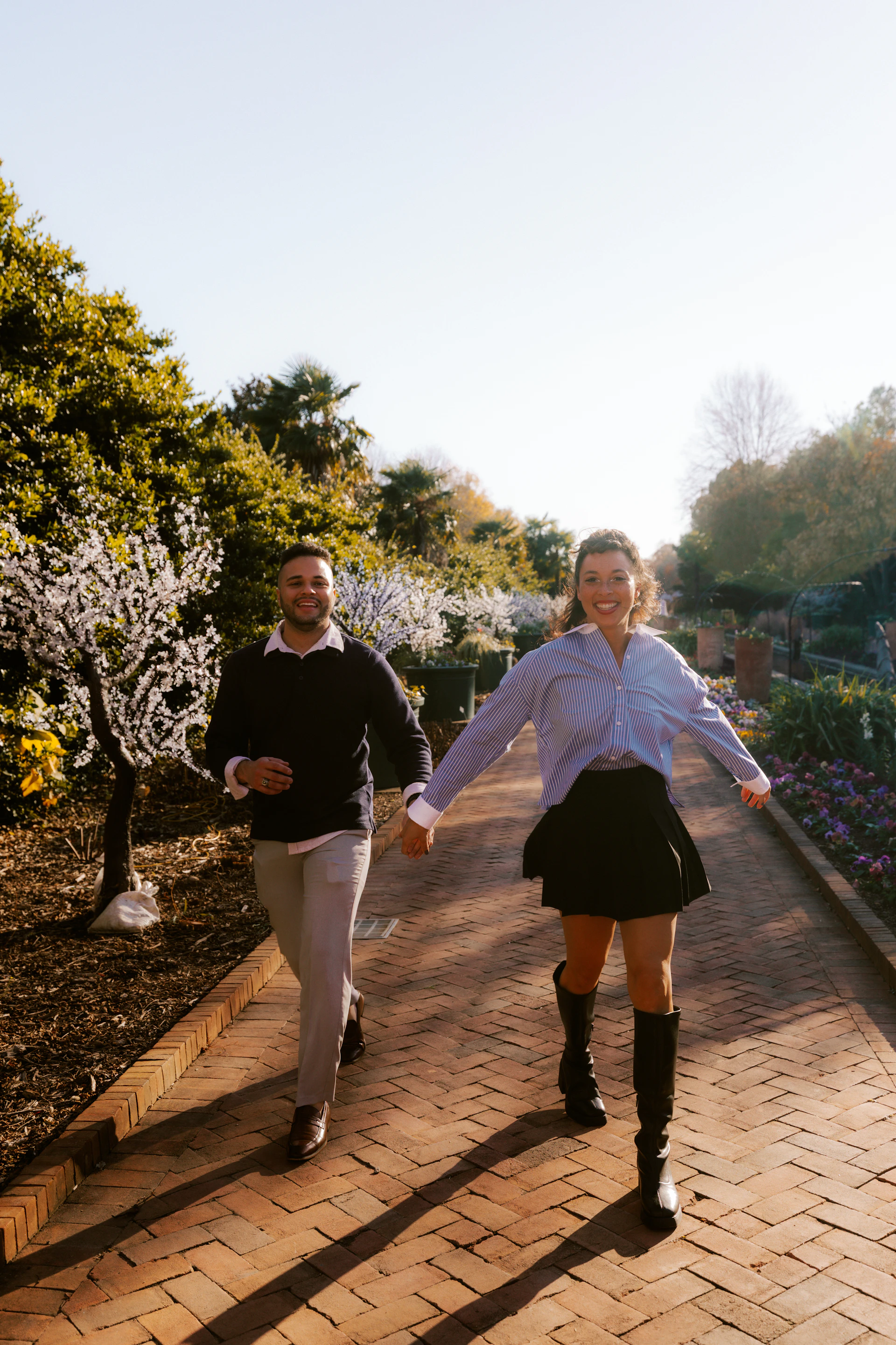 Couple holding hands walking on brick path in park.