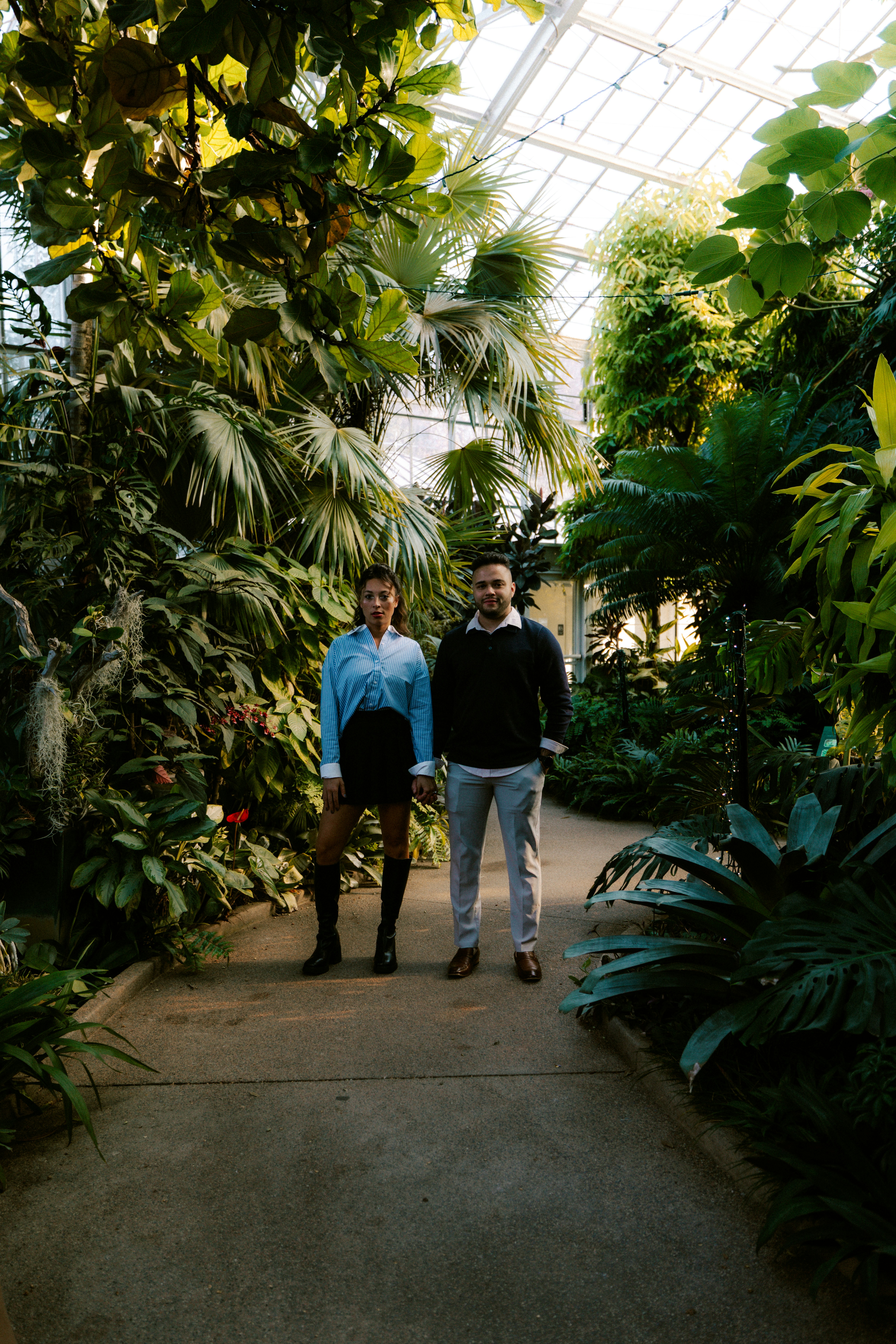 Couple standing in a lush greenhouse surrounded by plants.