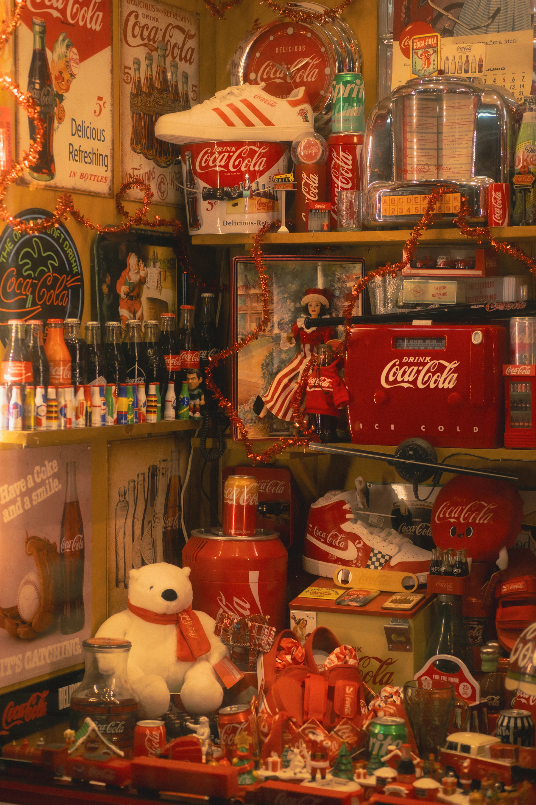 Shelves crowded with Coca-Cola memorabilia: tin signs, bottles, cans, a toy cooler, a polar bear and a model train