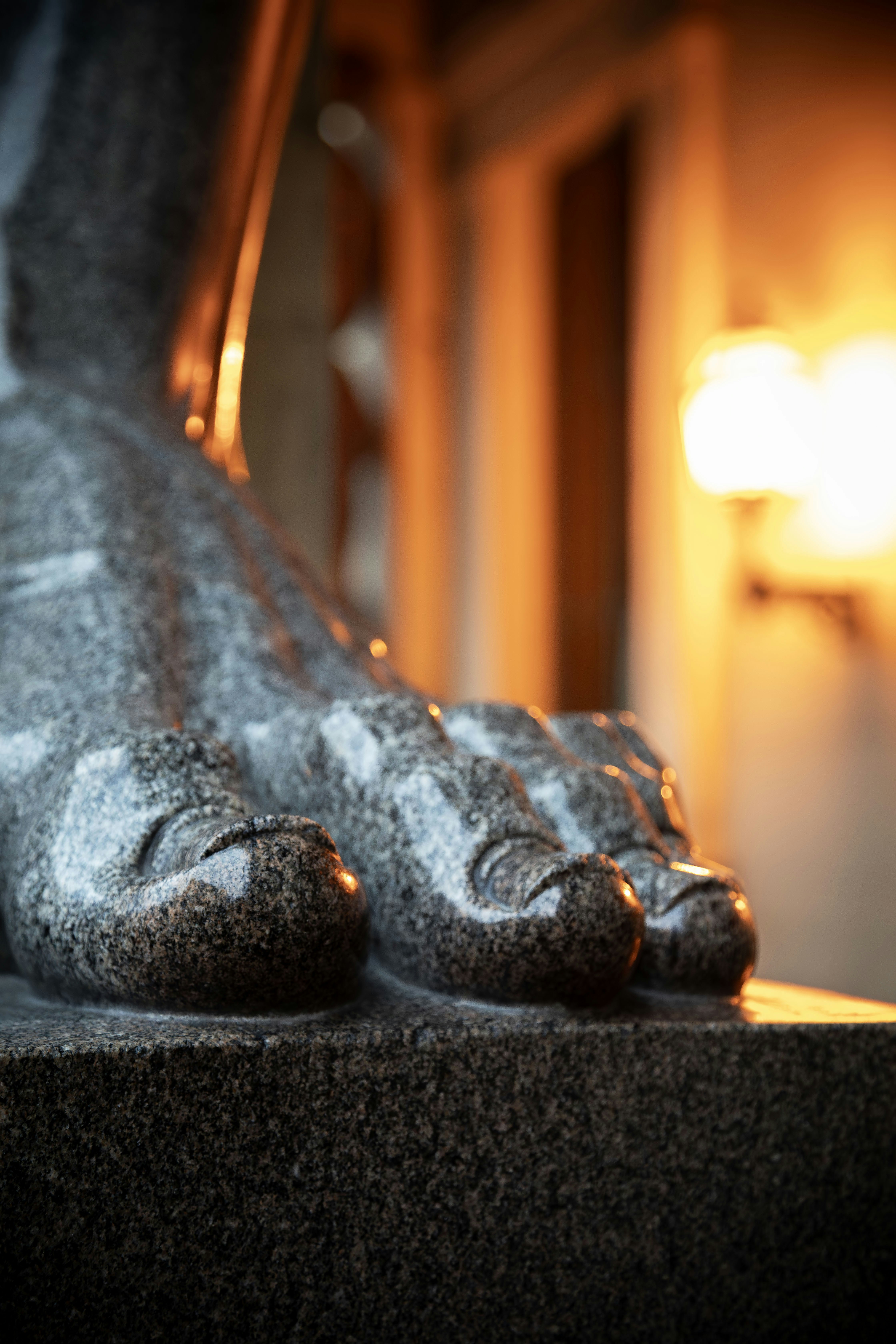Close up of a granite statue's foot with warm light