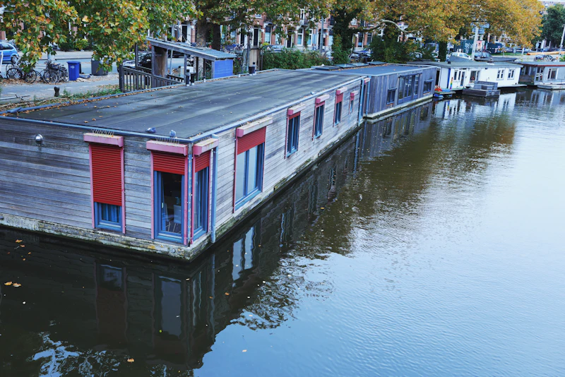 A long houseboat with red shutters moored along a canal at dusk
