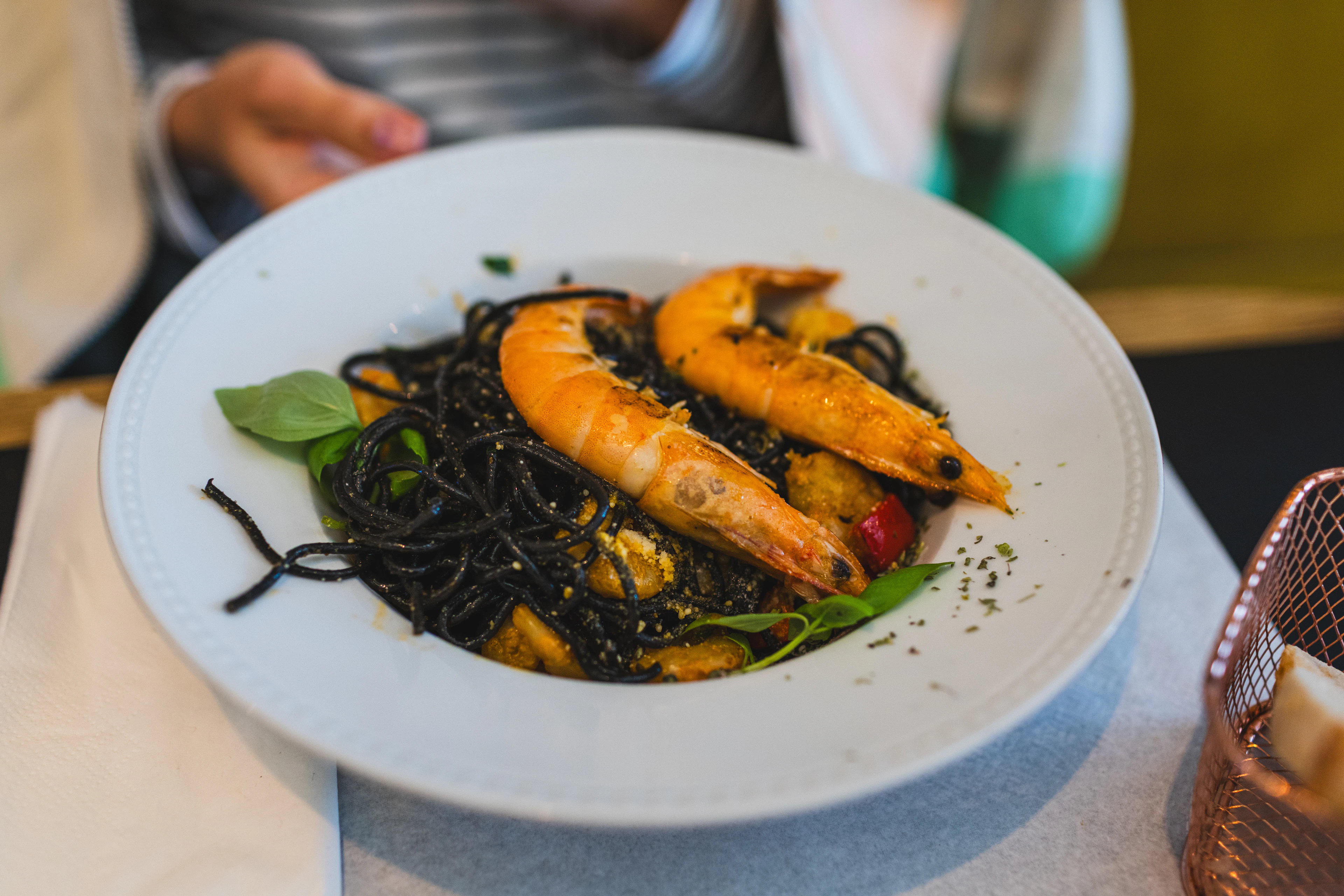 Black squid-ink pasta with whole prawns and basil on a white plate