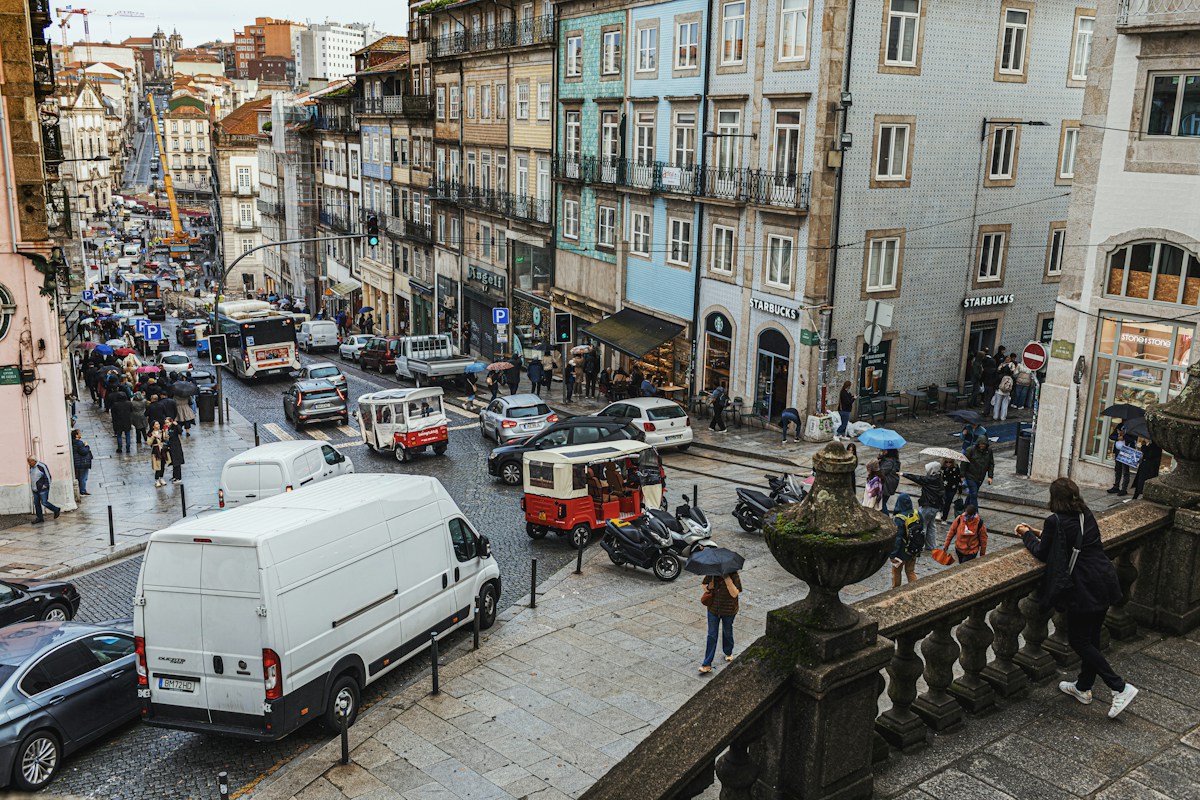 Rue en pente de Porto sous la pluie, avec un tramway rouge, des voitures et des passants munis de parapluies entre des façades colorées